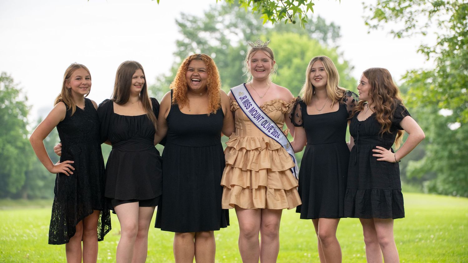 Group wearing black dresses standing outdoors in a grassy field.