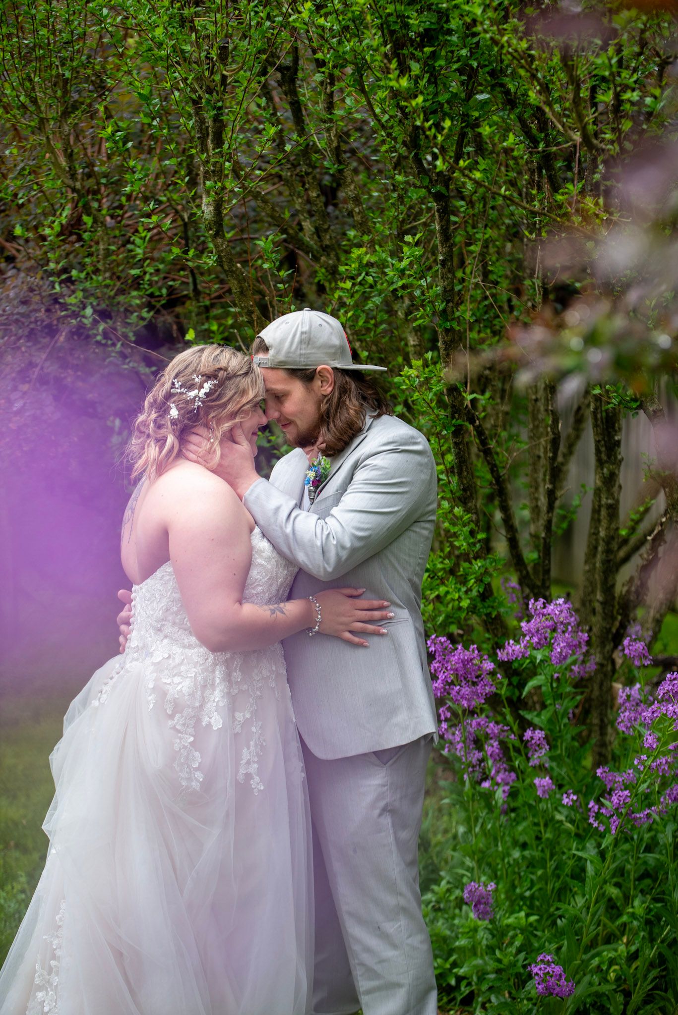 A romantic wedding moment in a garden with purple flowers and greenery.