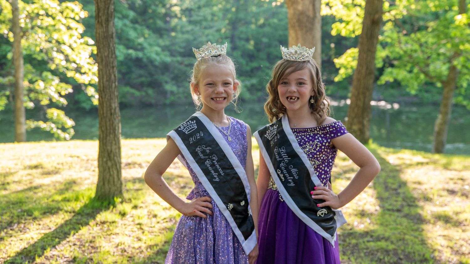 Pageant winners with crowns and sashes share candid moments in a forest setting.