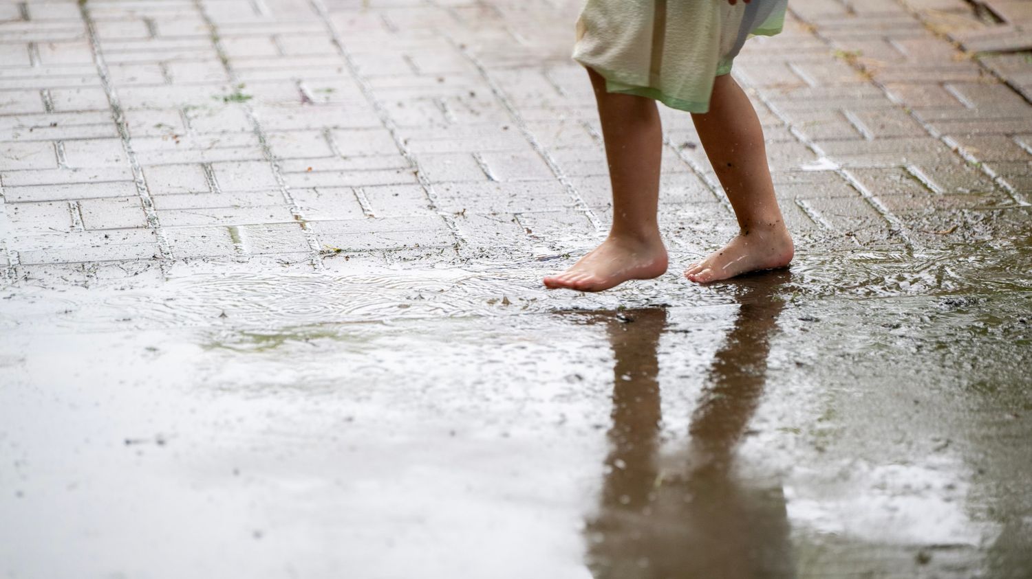 Close-up of bare feet walking on wet pavement with puddles.