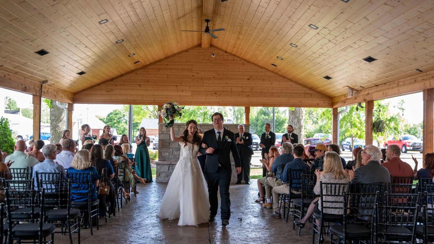 Panoramic view of a rustic wooden ceiling venue set up with black chairs for a wedding ceremony.
