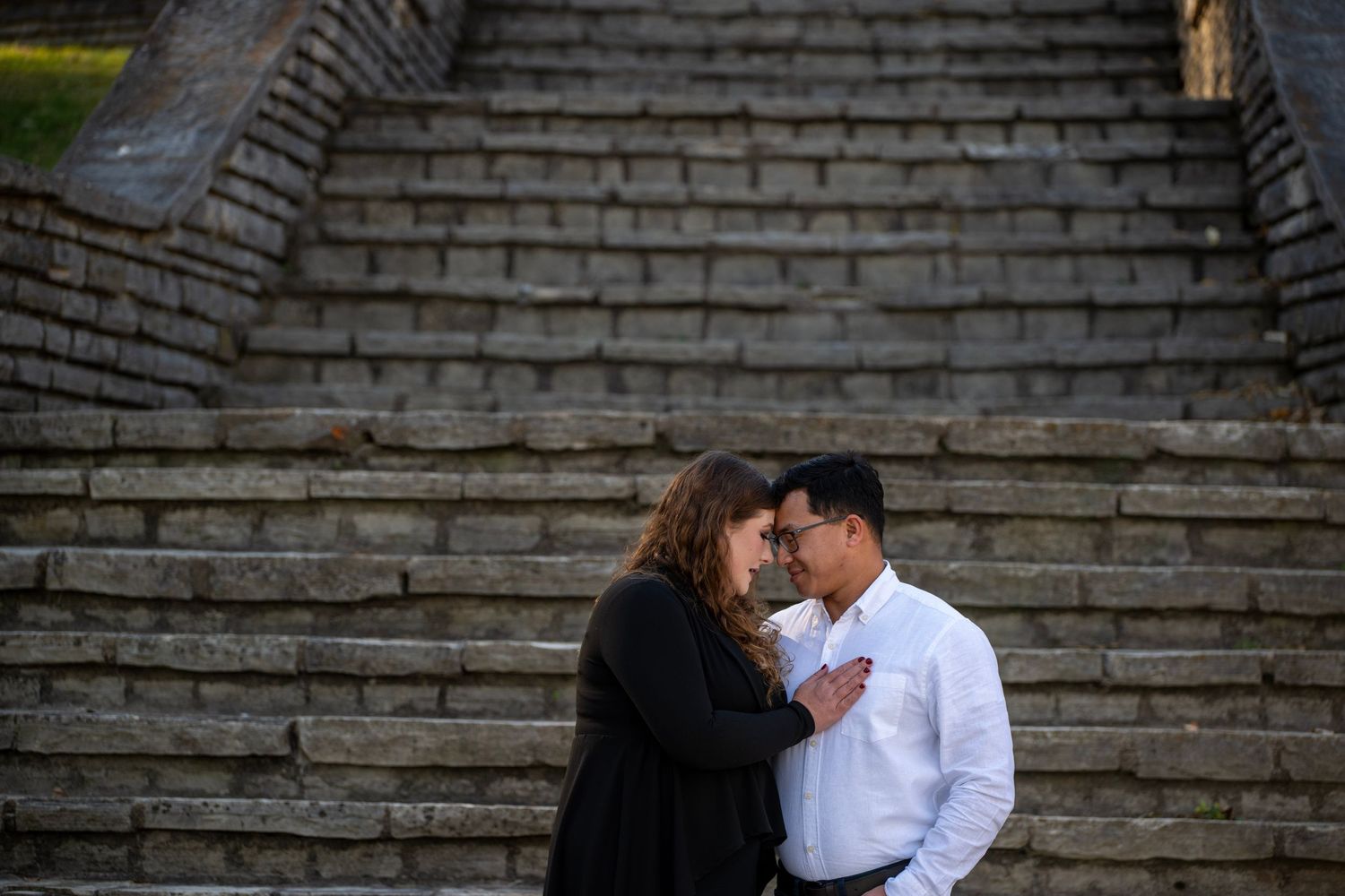 Romantic couple embraces on stone steps during an engagement photoshoot.