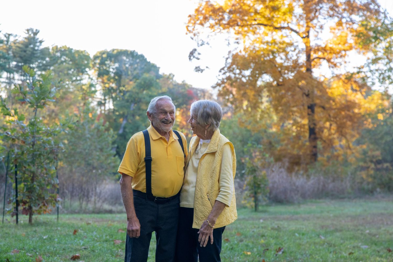 Couple in coordinating yellow outfits standing together in an autumn field at sunset.