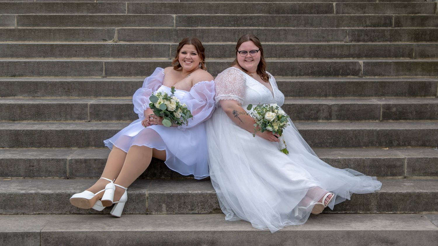 Wedding couple seated on grand stone steps of historic building.
