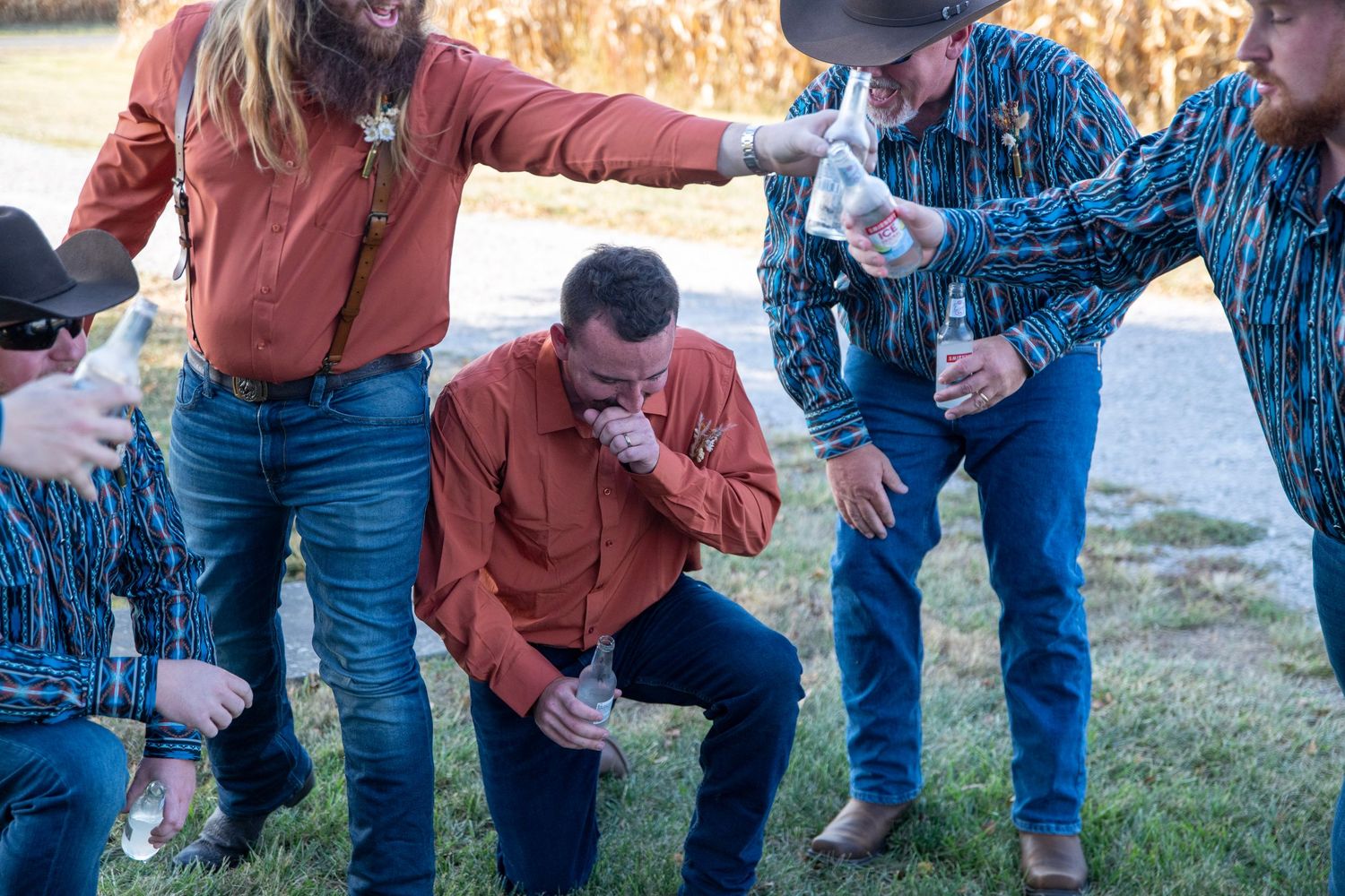 People in western wear and cowboy hats gather for drinks outdoors.