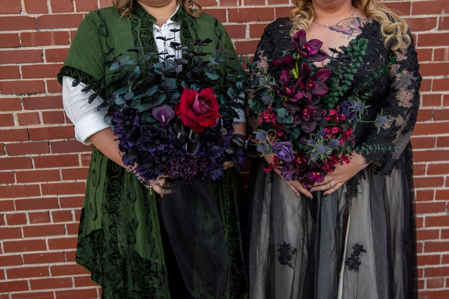 Wedding party holding vibrant purple and red bouquets against brick wall backdrop.