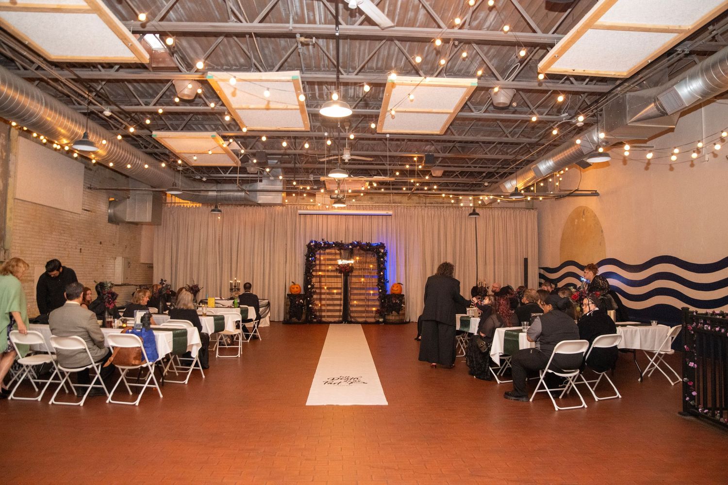 Large event space with rows of tables and chairs under industrial ceiling lighting.