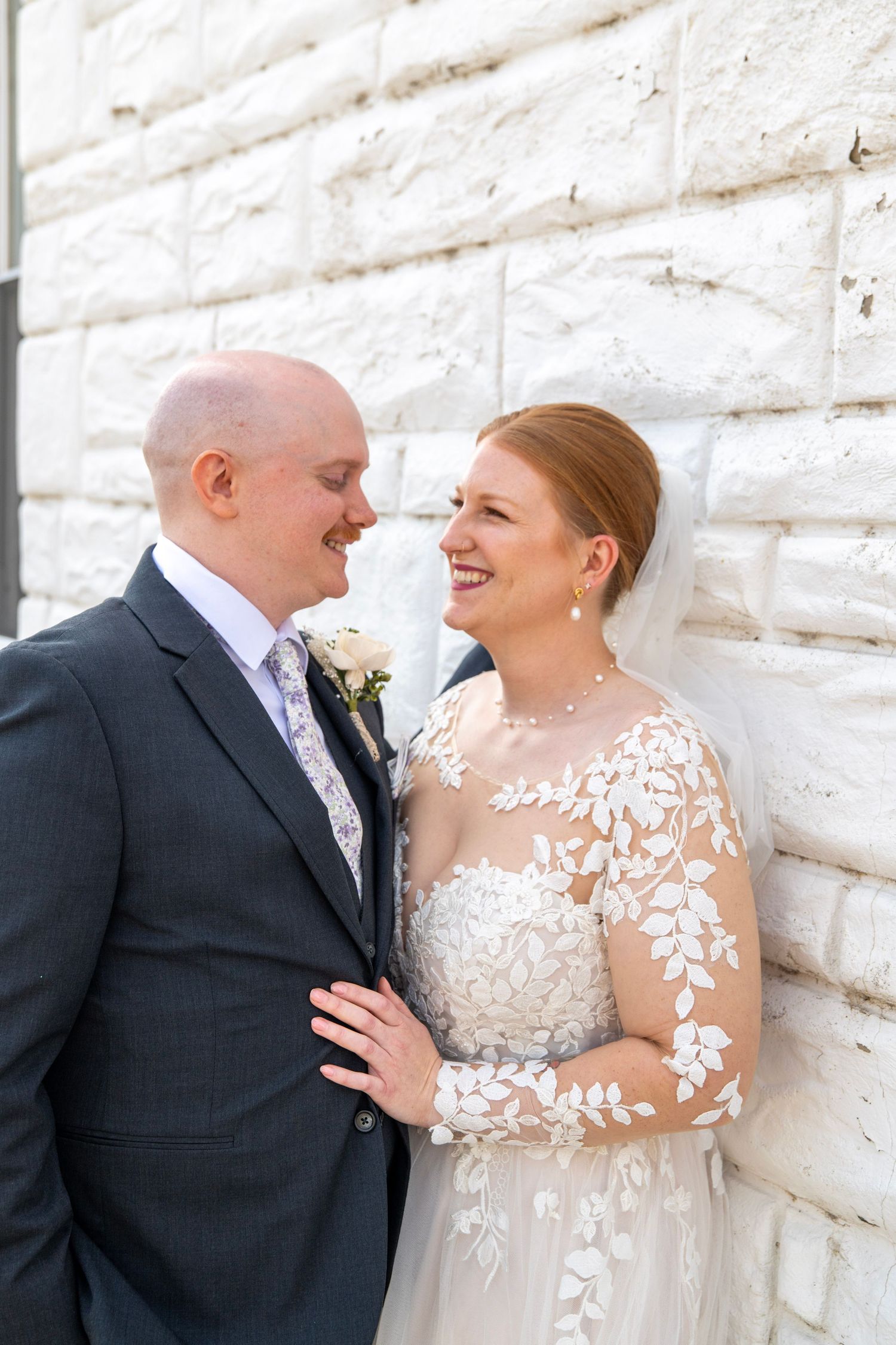 A couple shares romantic moments against a white stone wall during their wedding photoshoot.