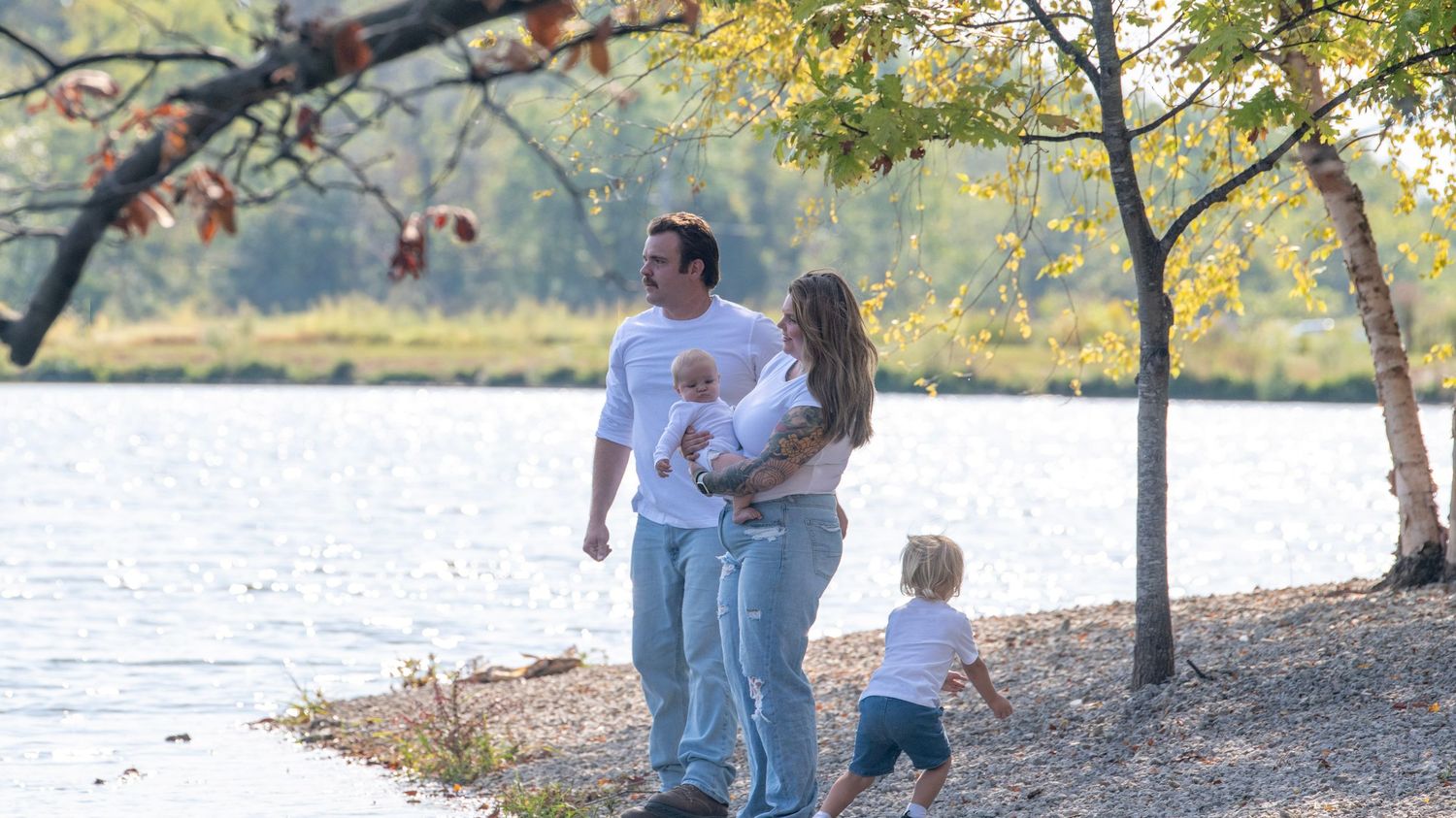 Family spending time together under fall trees near peaceful lakeside.