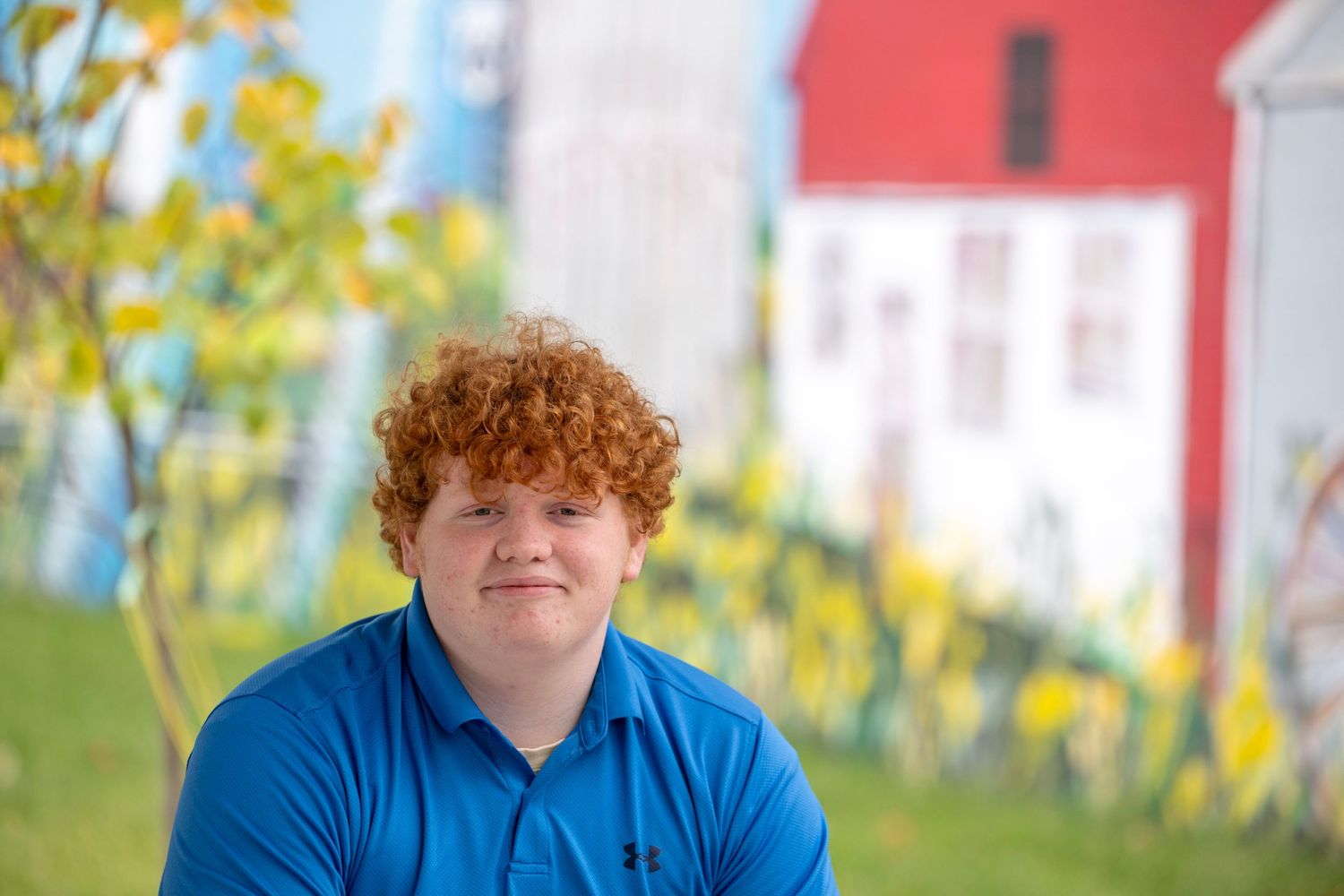 Person in blue shirt standing in front of red barn on sunny autumn day.