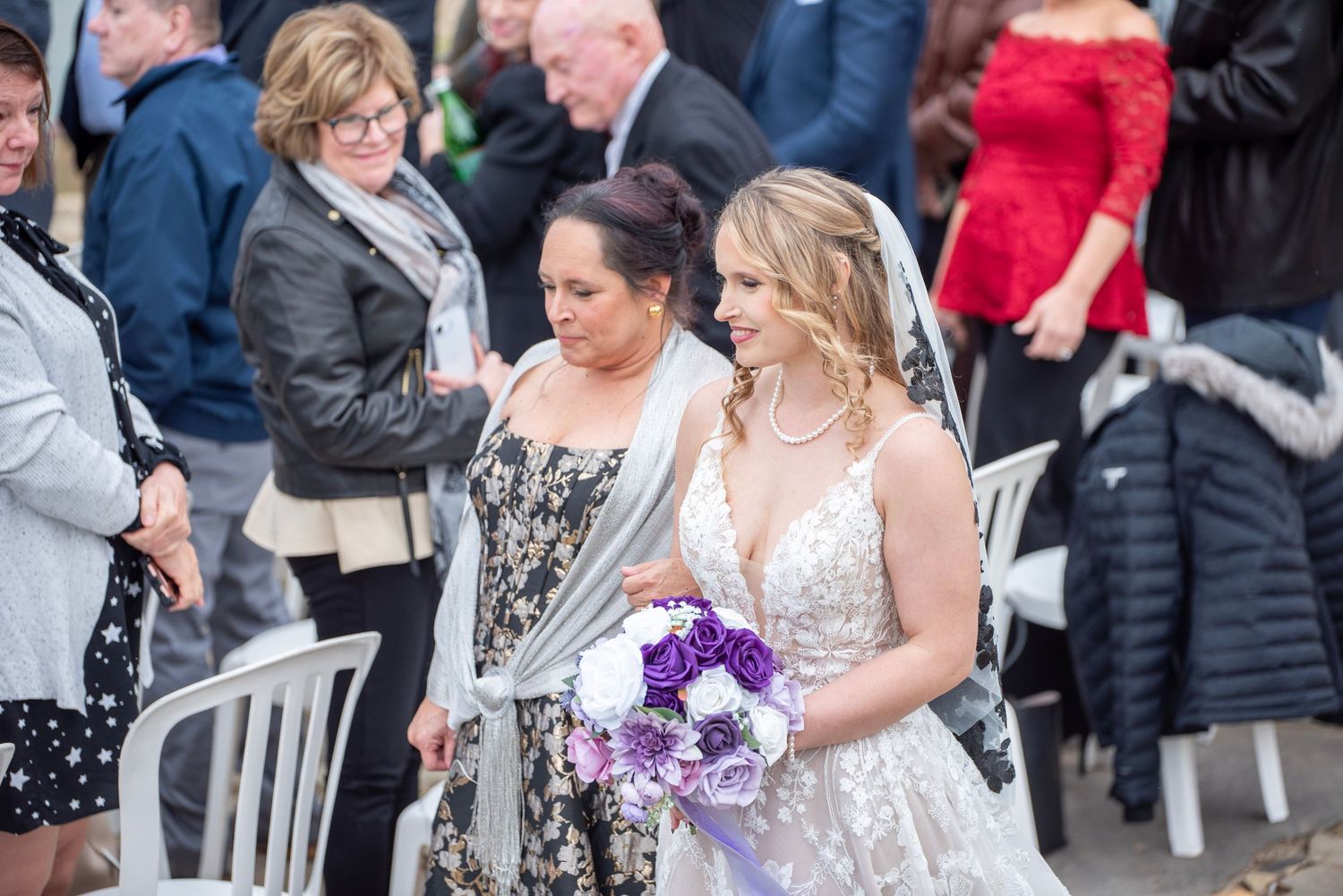 Wedding guests mingling outside venue wearing formal attire in winter coats.