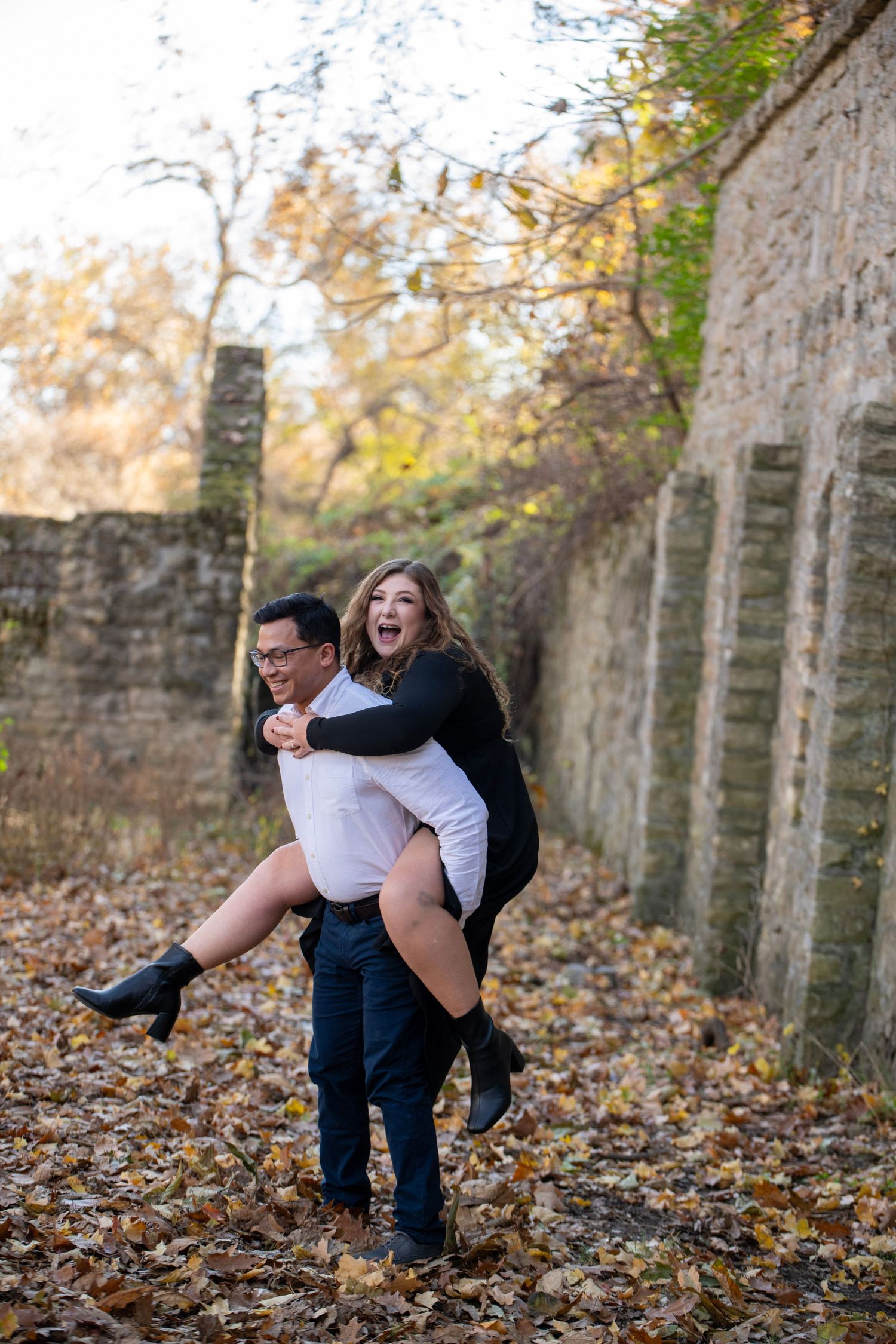 Couple creates fun moment with piggyback ride near historic stone ruins in fall setting.