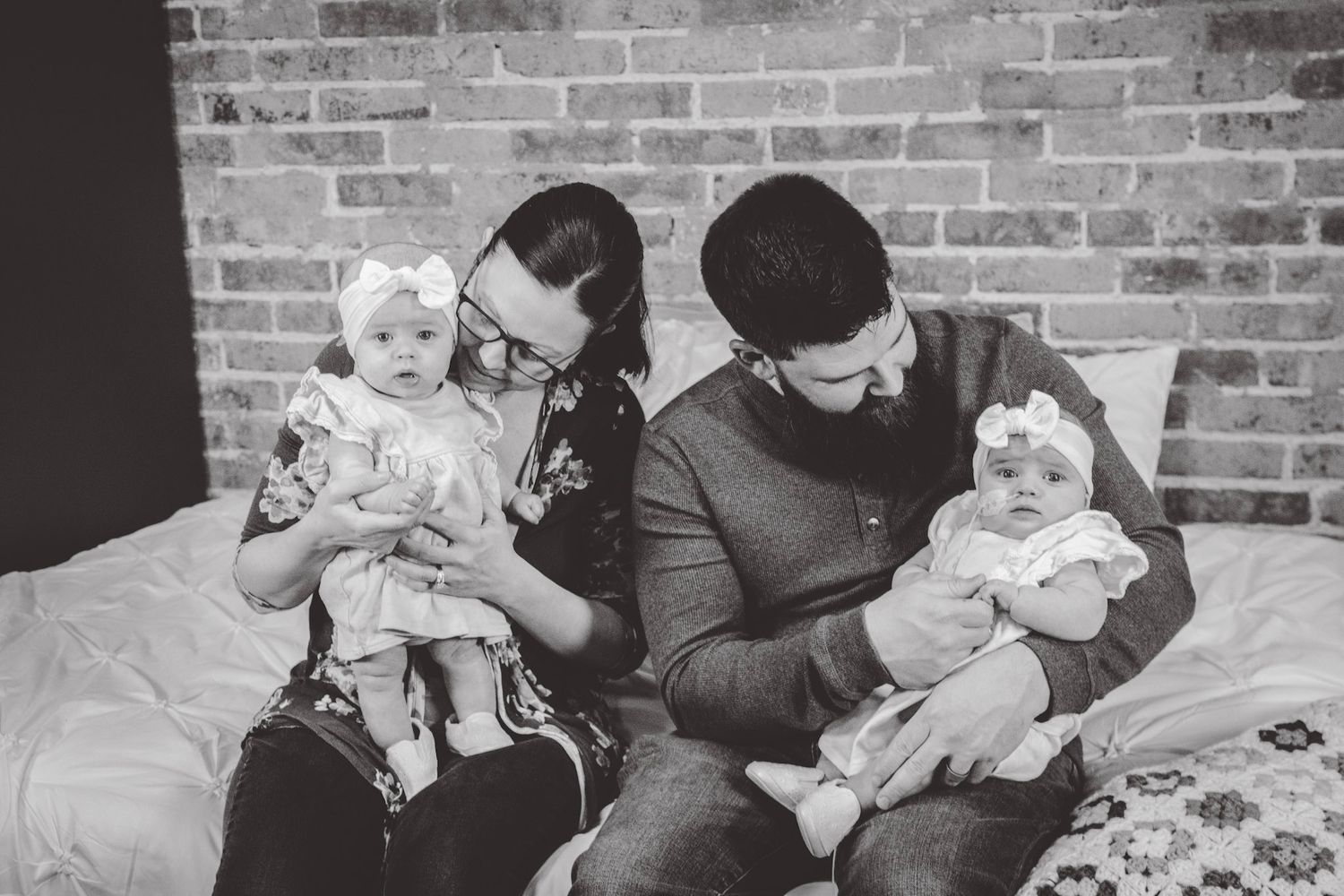 Black and white portrait of family with twins sitting on couch with patterned quilt.