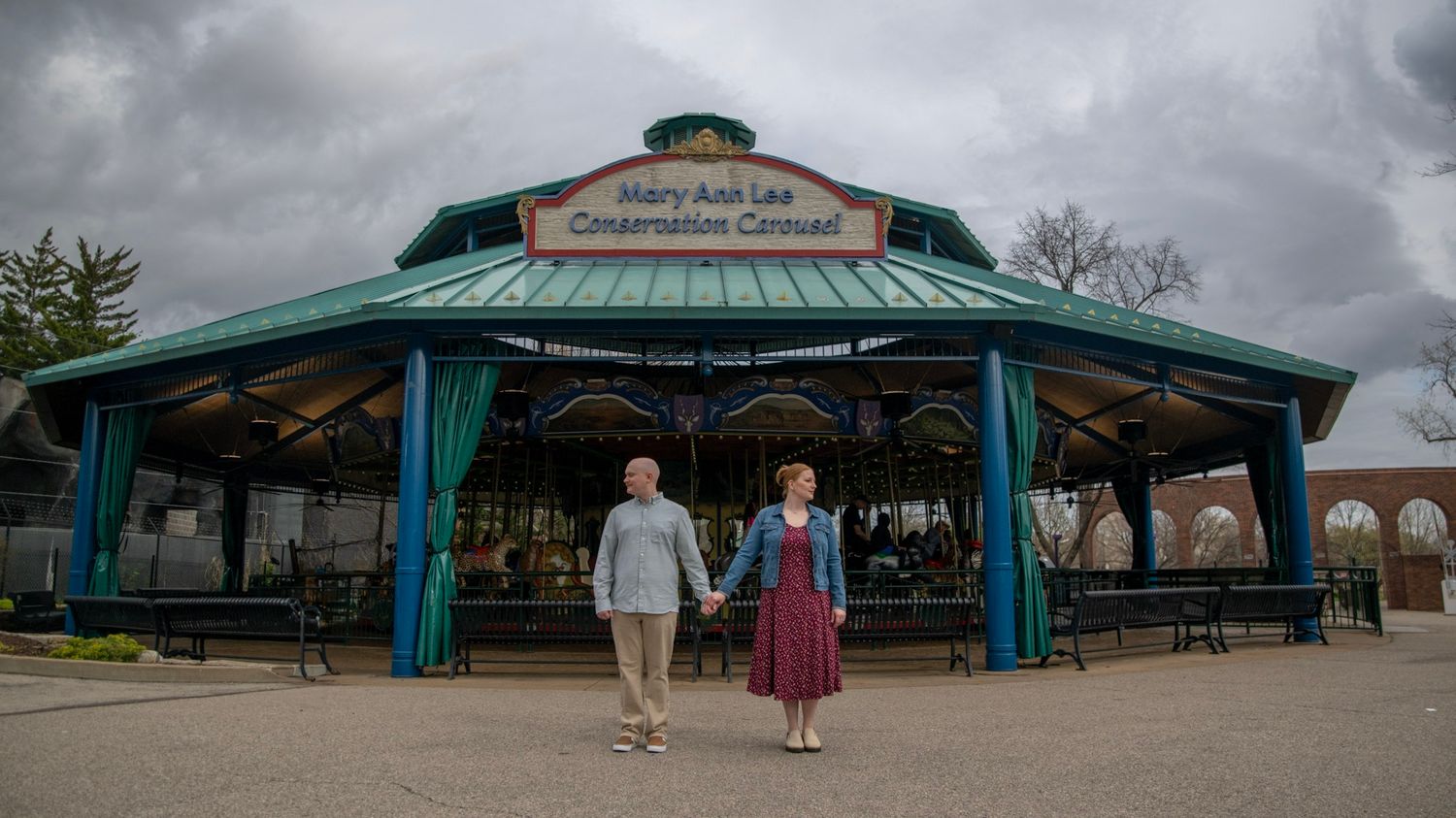 A couple approaches a teal-roofed pavilion under stormy skies.