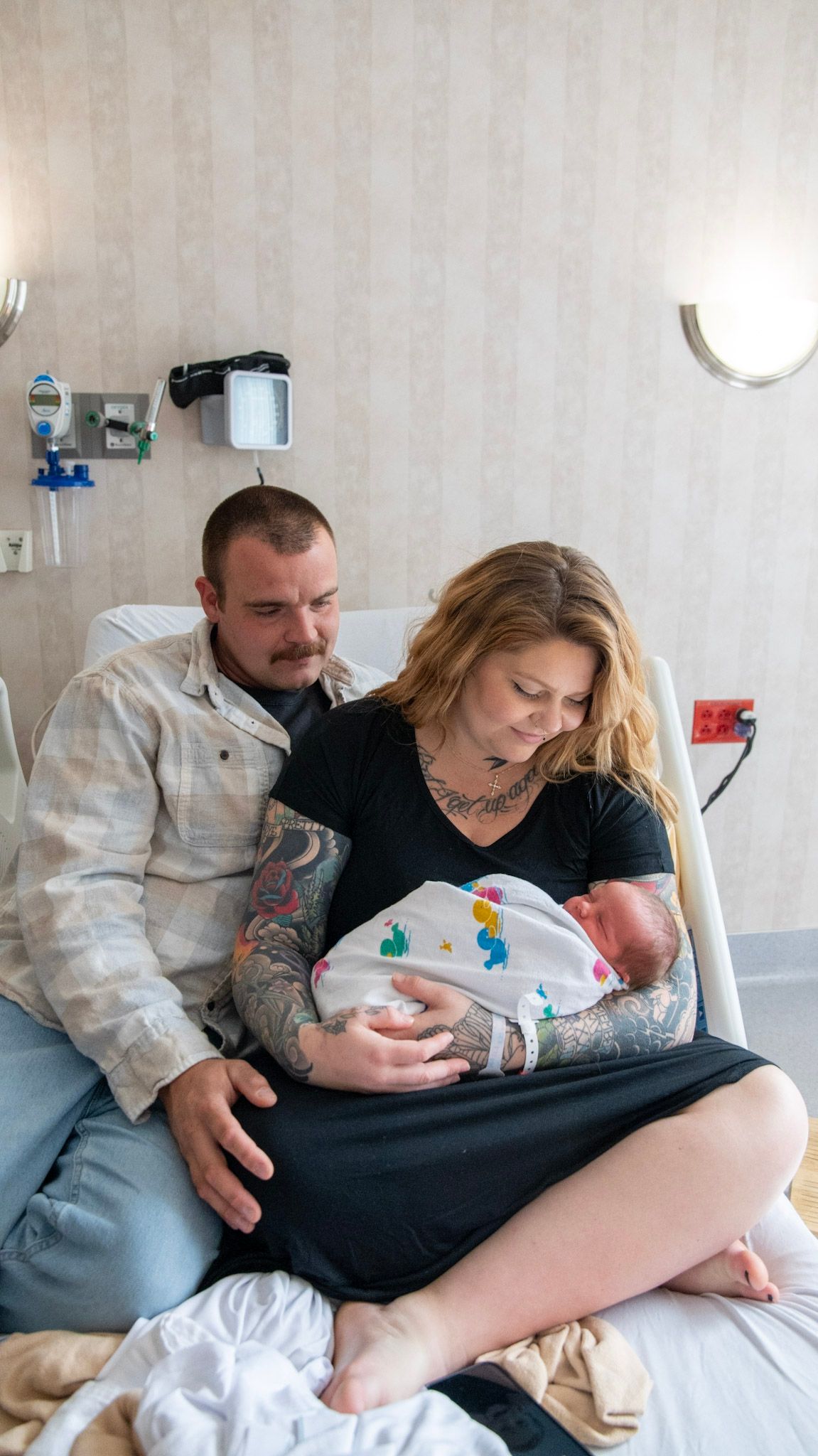 A tender moment in a hospital room as new parents bond with their newborn baby wrapped in a blanket.