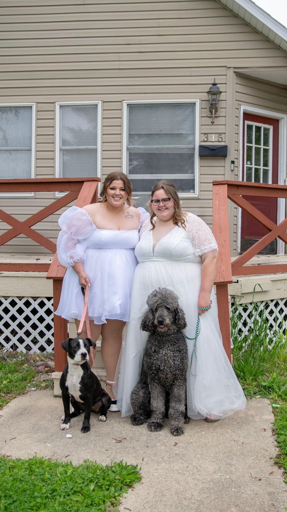 Two dogs sitting on a concrete porch next to people in white dresses.