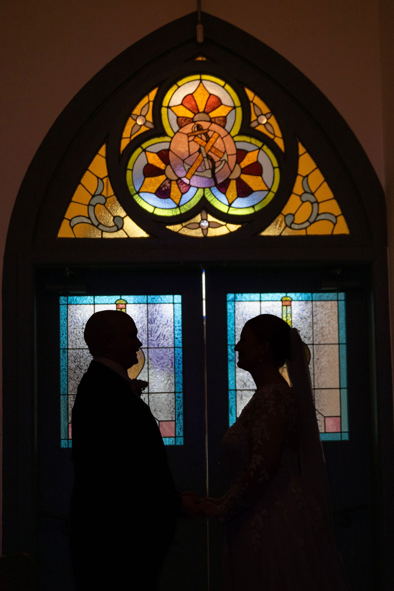 Silhouettes against stained glass church windows during a wedding ceremony.