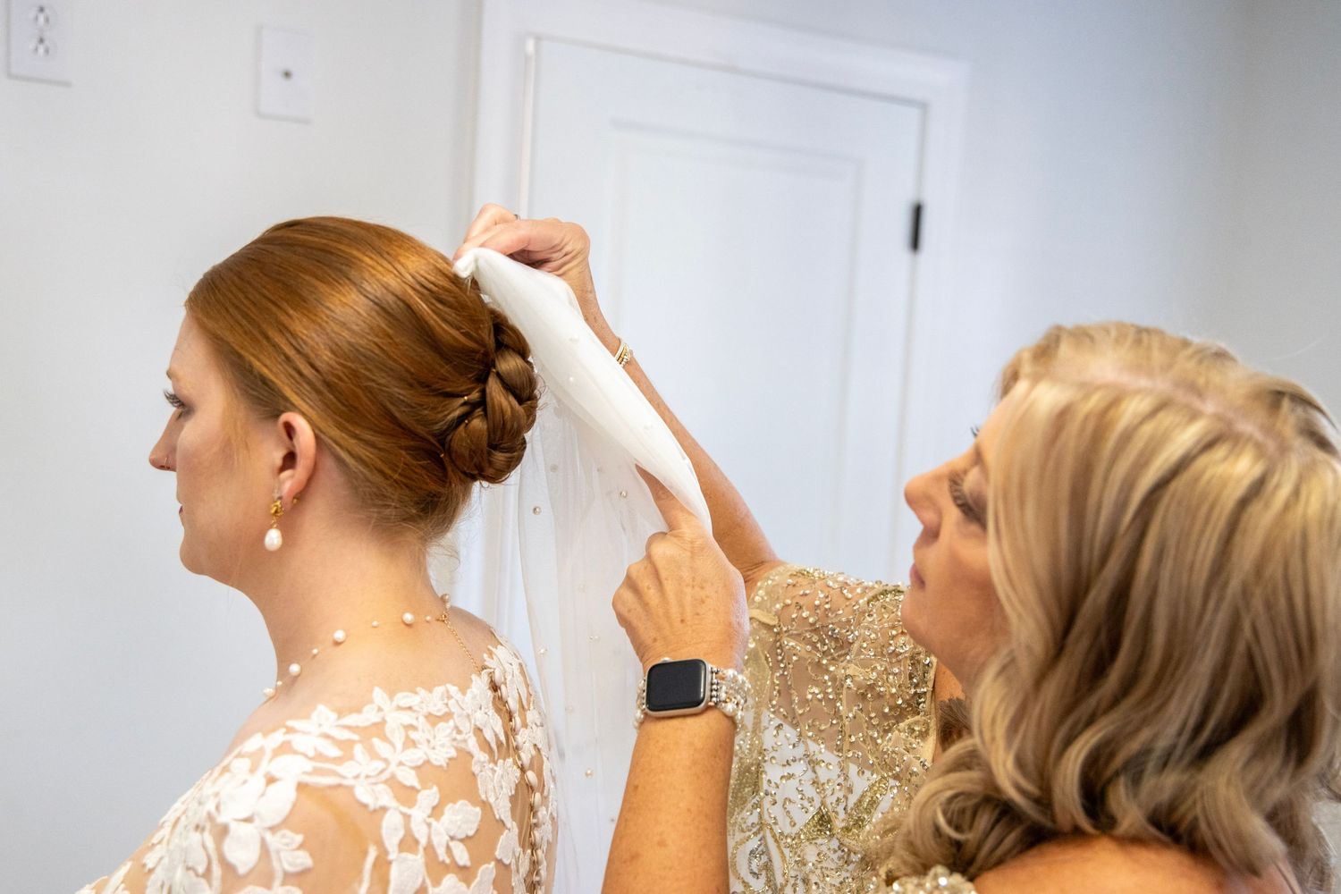 Bridesmaids in shimmering champagne dresses help with wedding preparations in a bright room.