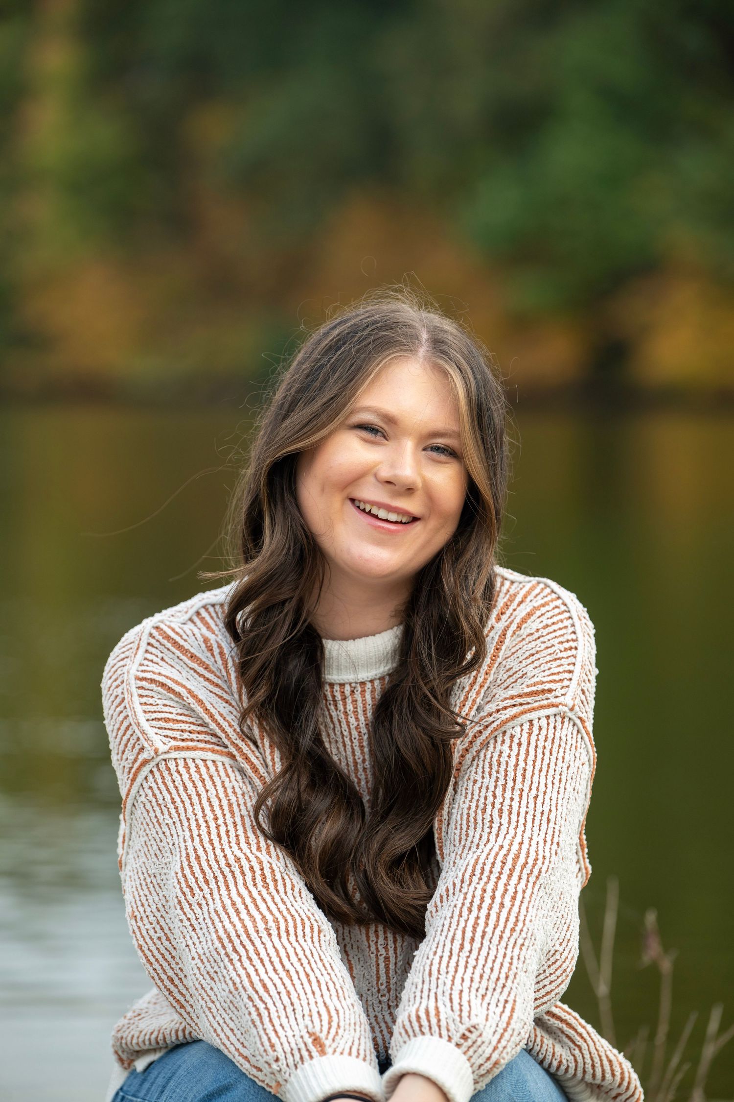 Person in striped sweater sitting by lake with autumn foliage reflection in water.
