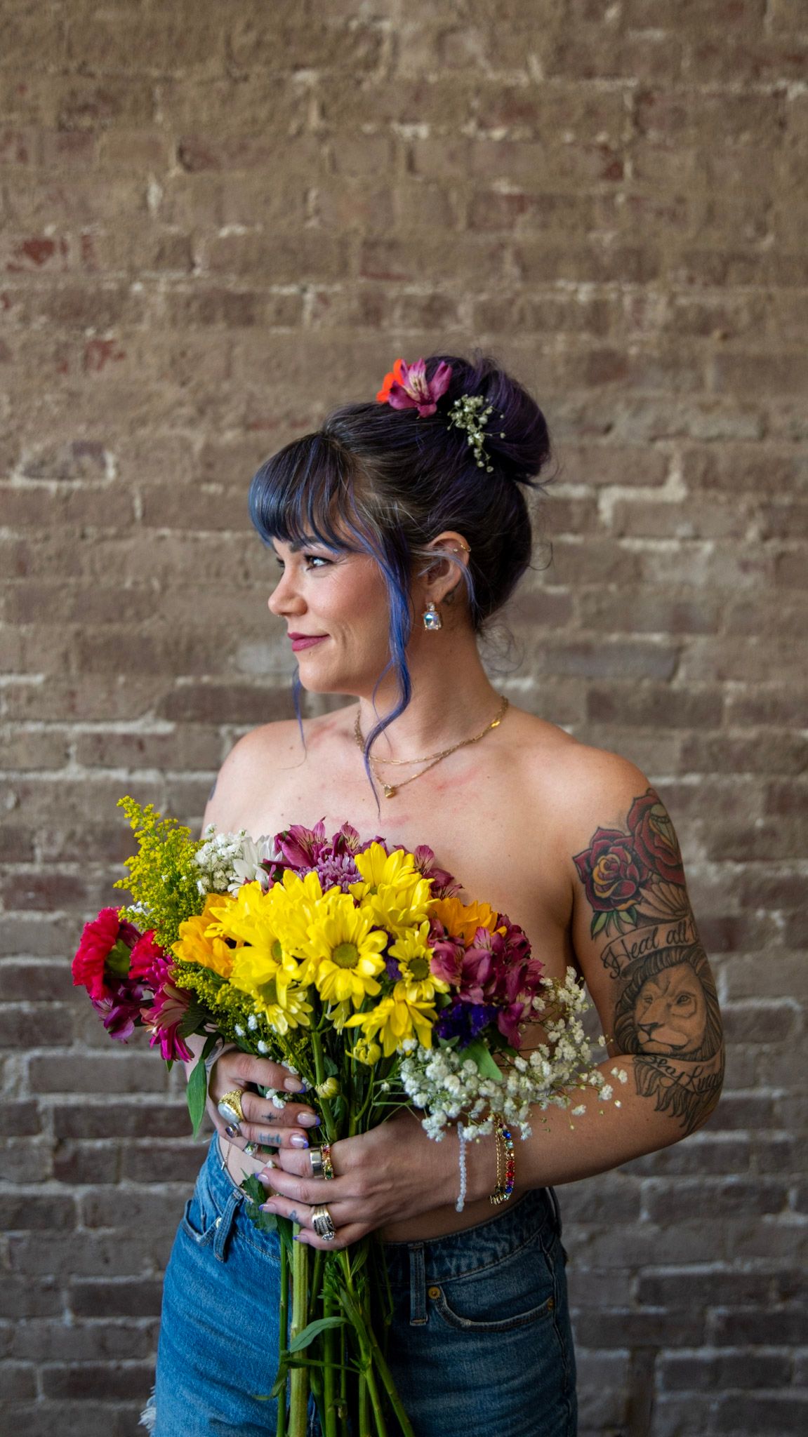 Person with updo hairstyle holding vibrant wildflower bouquet against brick background.