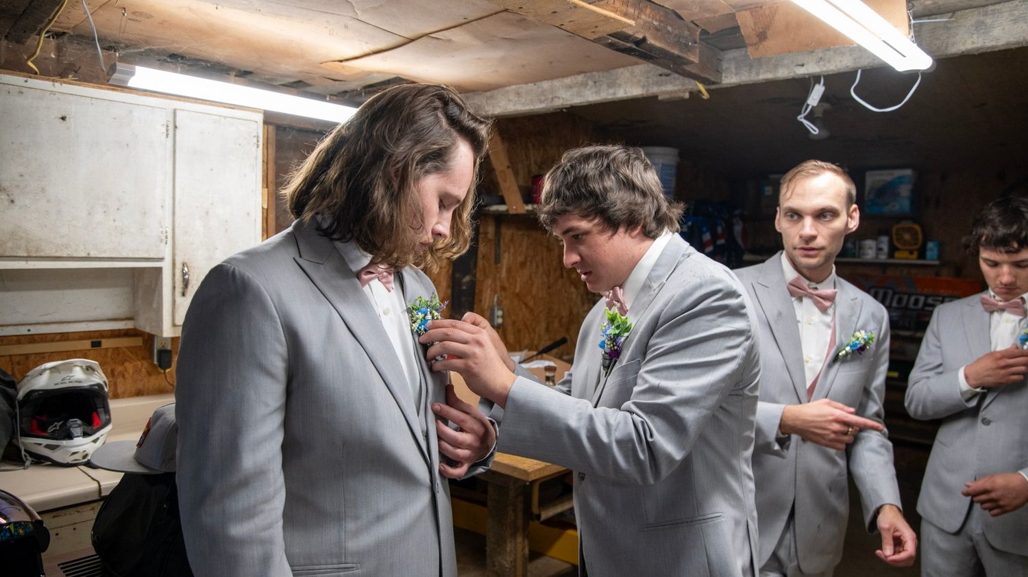 Groomsmen help adjust a tie in a basement setting before the ceremony.