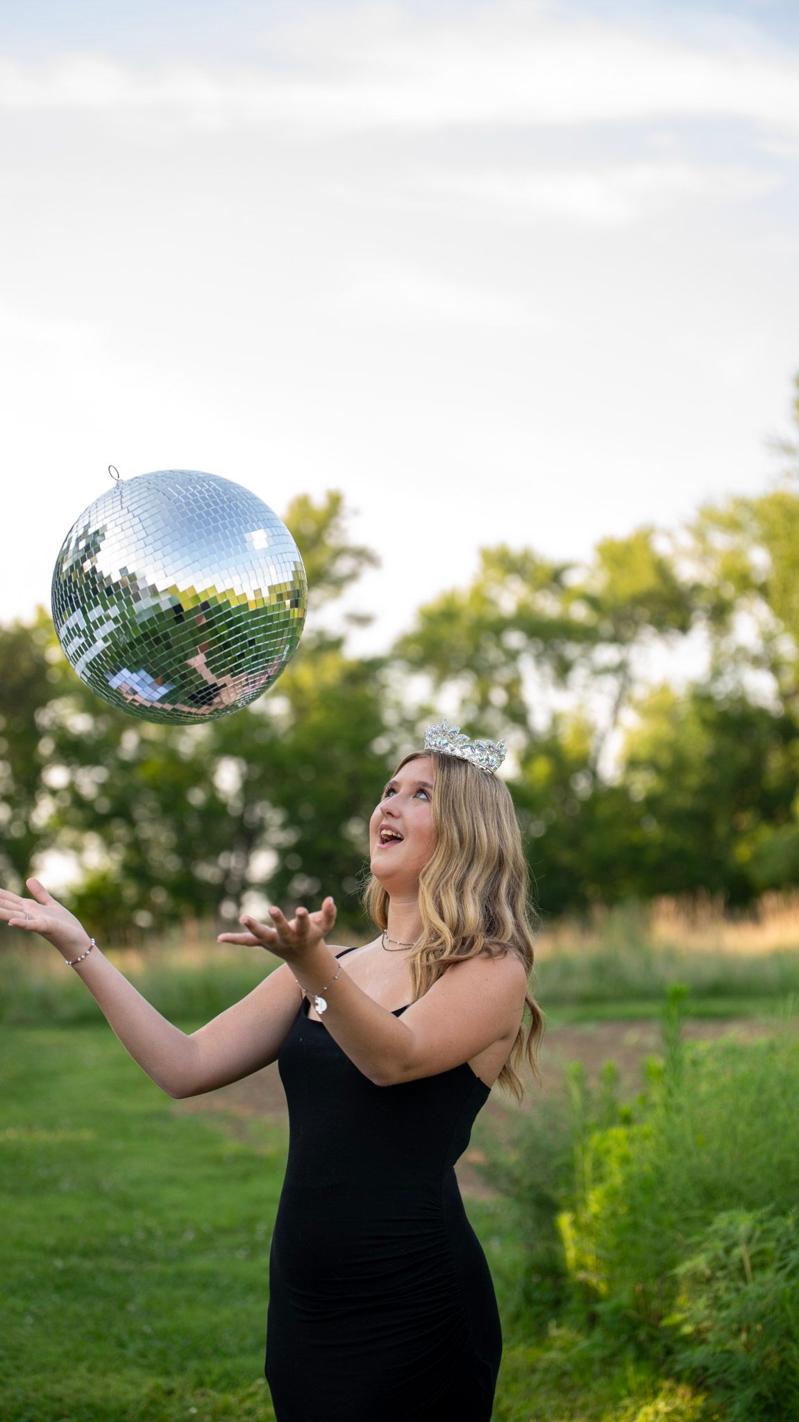 Playful outdoor portrait session with a disco ball and tiara against a natural backdrop.
