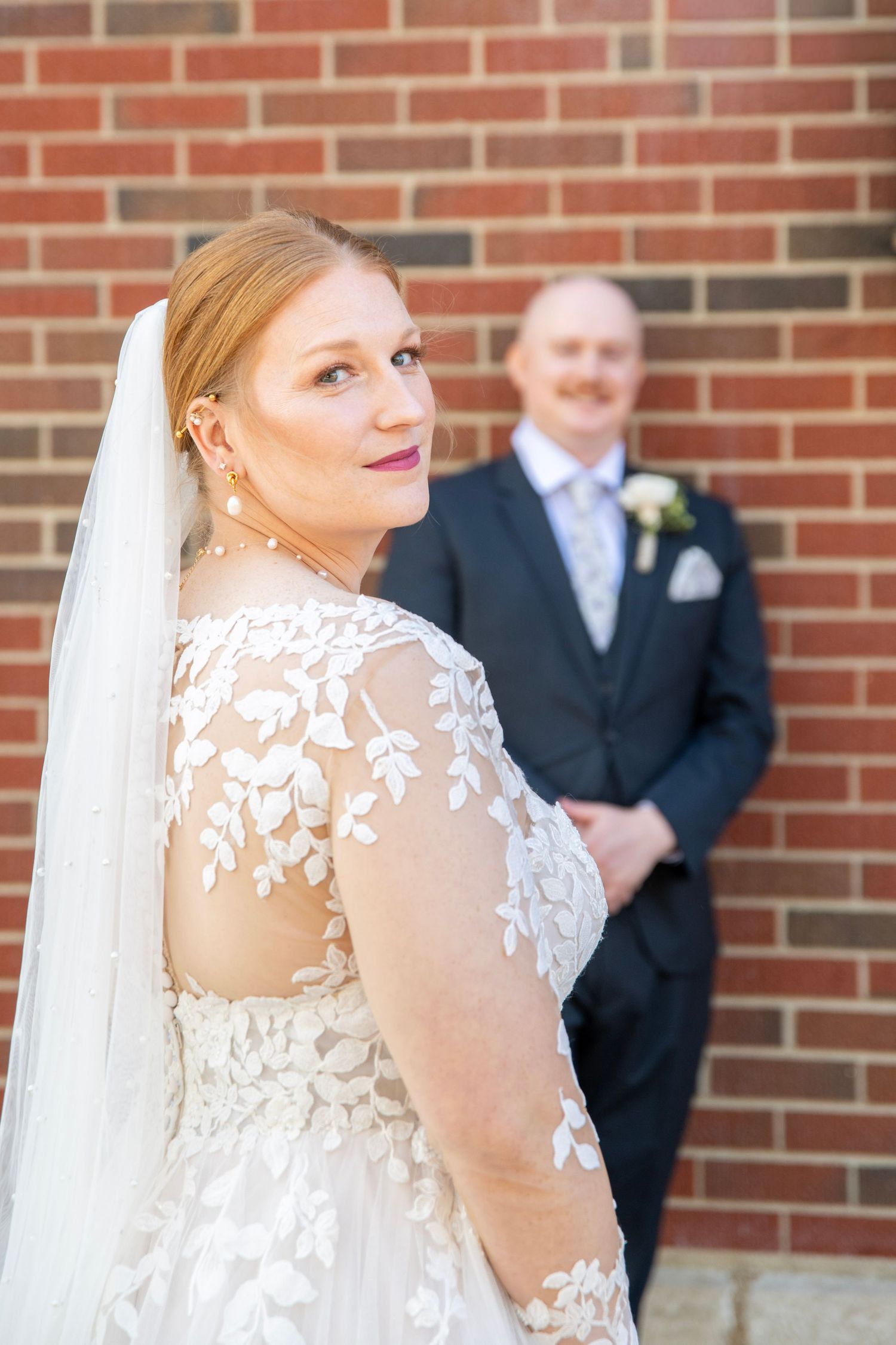 Bride in lace detailed dress with sheer back poses during outdoor wedding photoshoot.