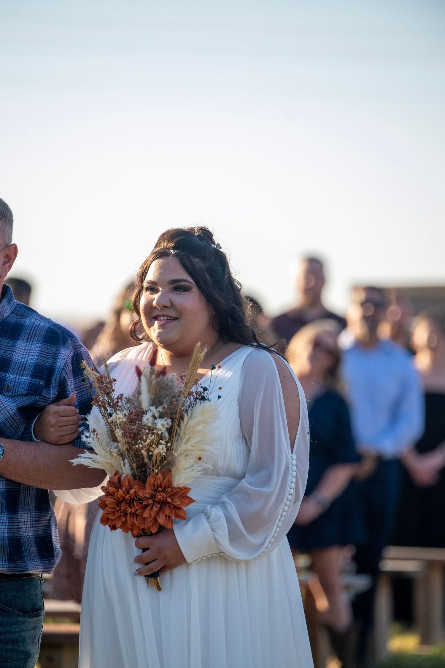 Wedding guests gather outdoors at sunset during a rustic countryside celebration.