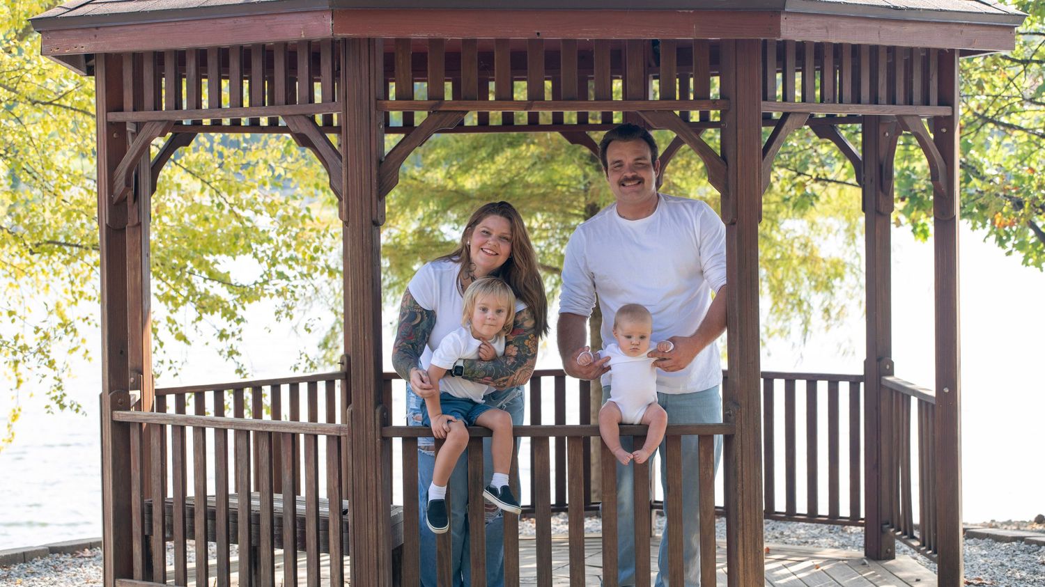 Family gathering under covered wooden pavilion by scenic lake.