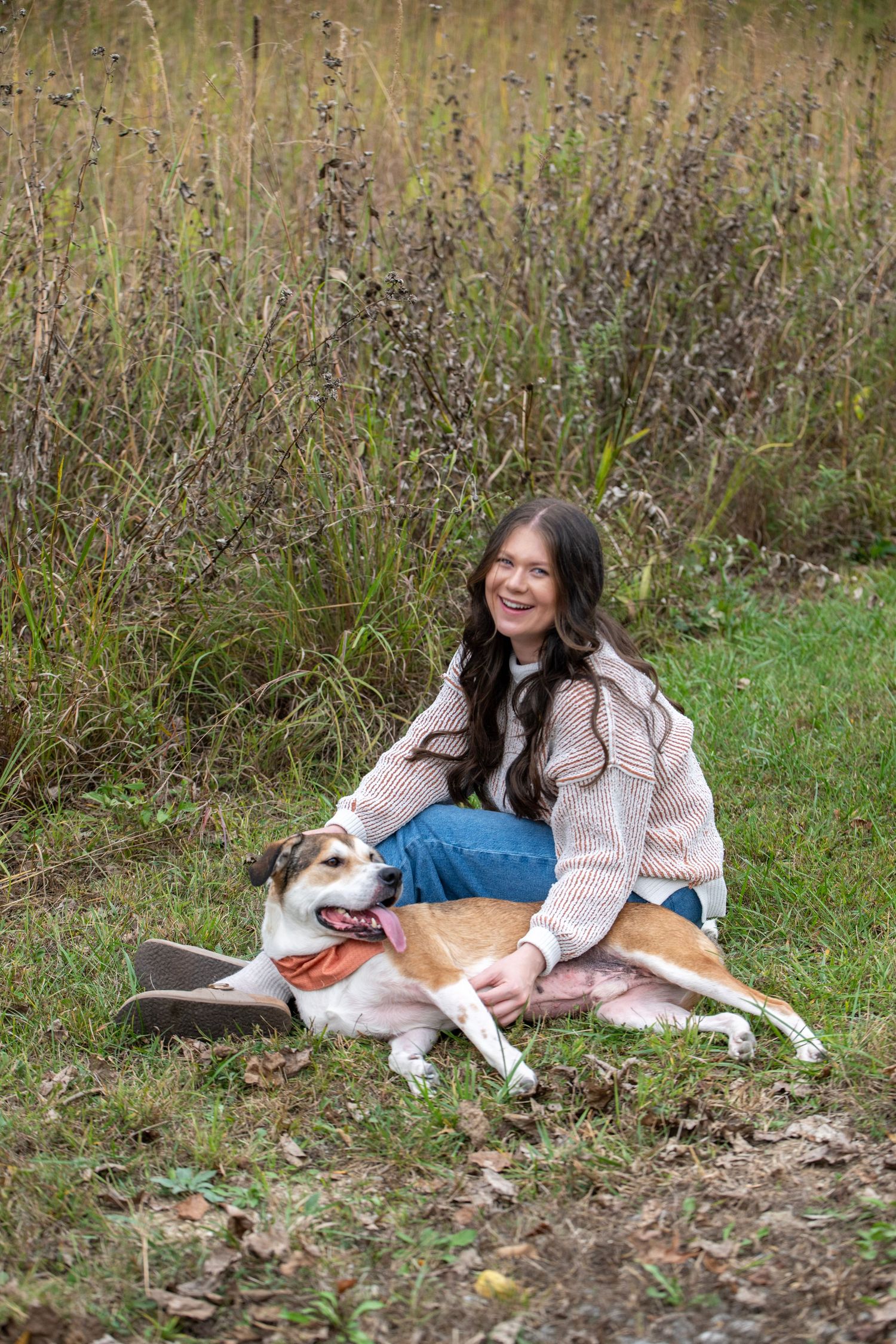 A relaxed outdoor portrait shows a person and their dog lounging in a natural setting.