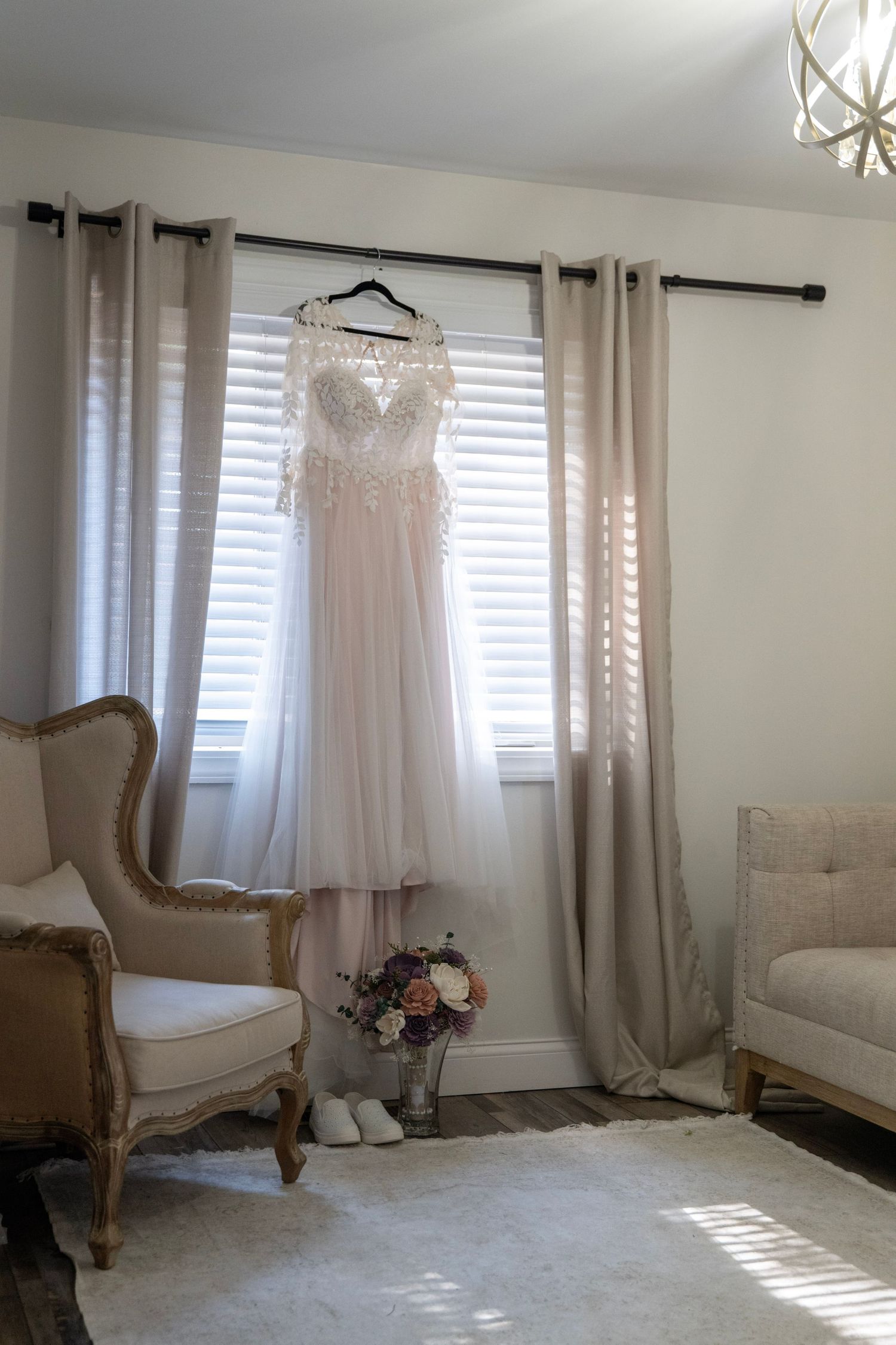 Elegant room interior with white curtains, upholstered chair and wedding dress on display.