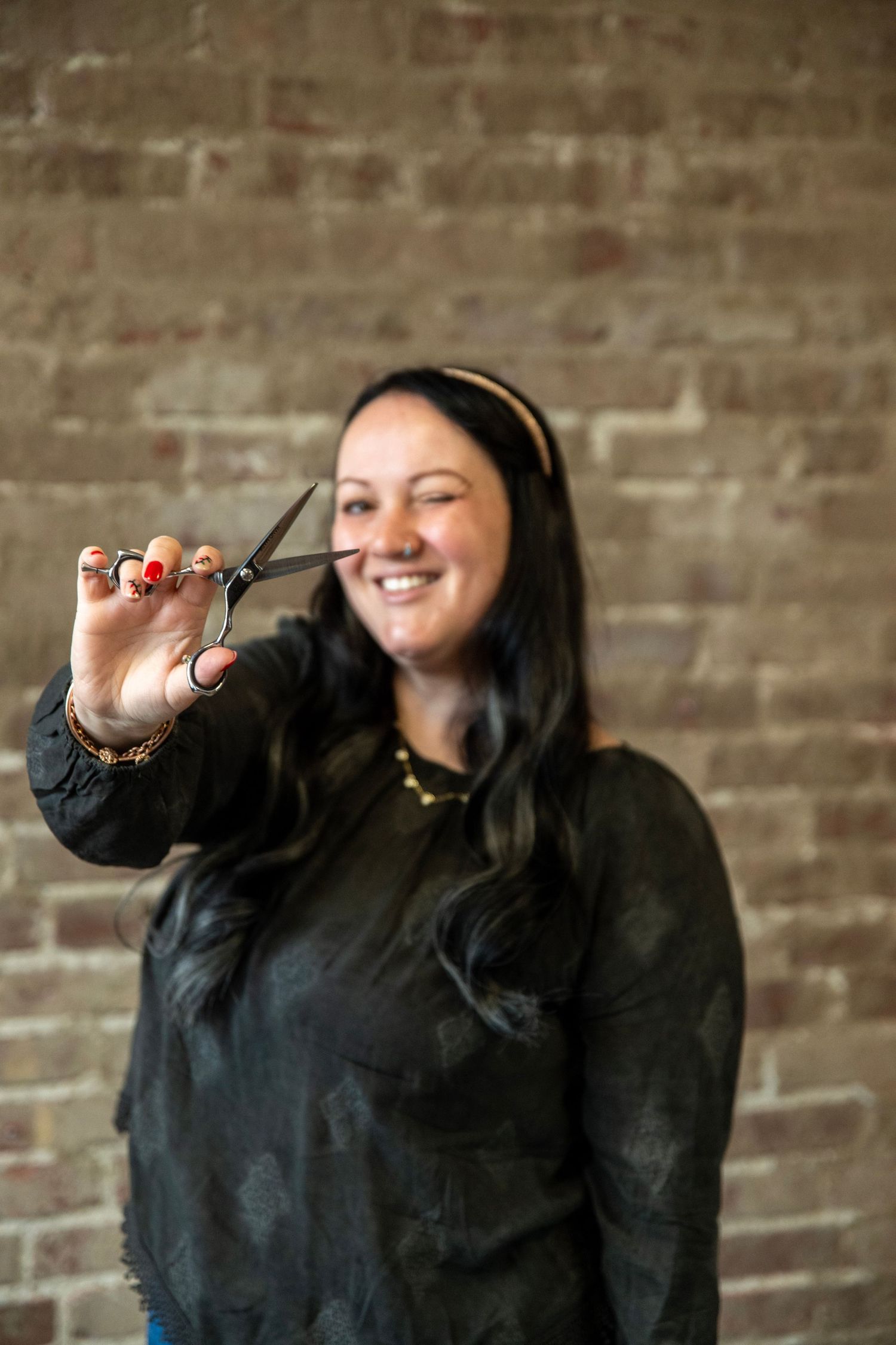 Person in black hoodie makes playful gestures against brick wall background.