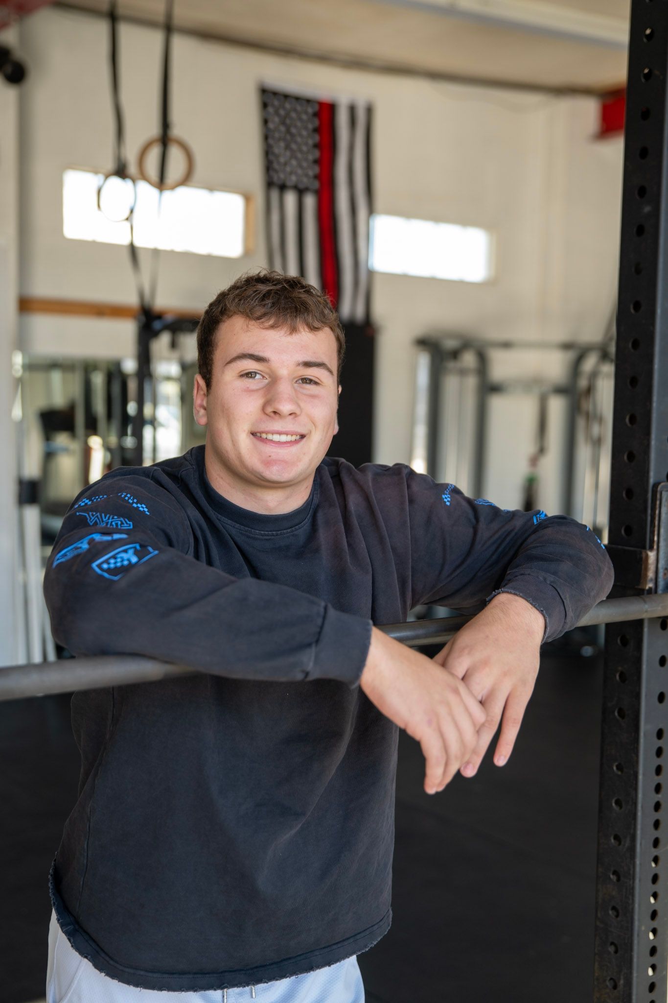 A person in a dark sweatshirt leans against exercise equipment in a bright indoor gym setting.