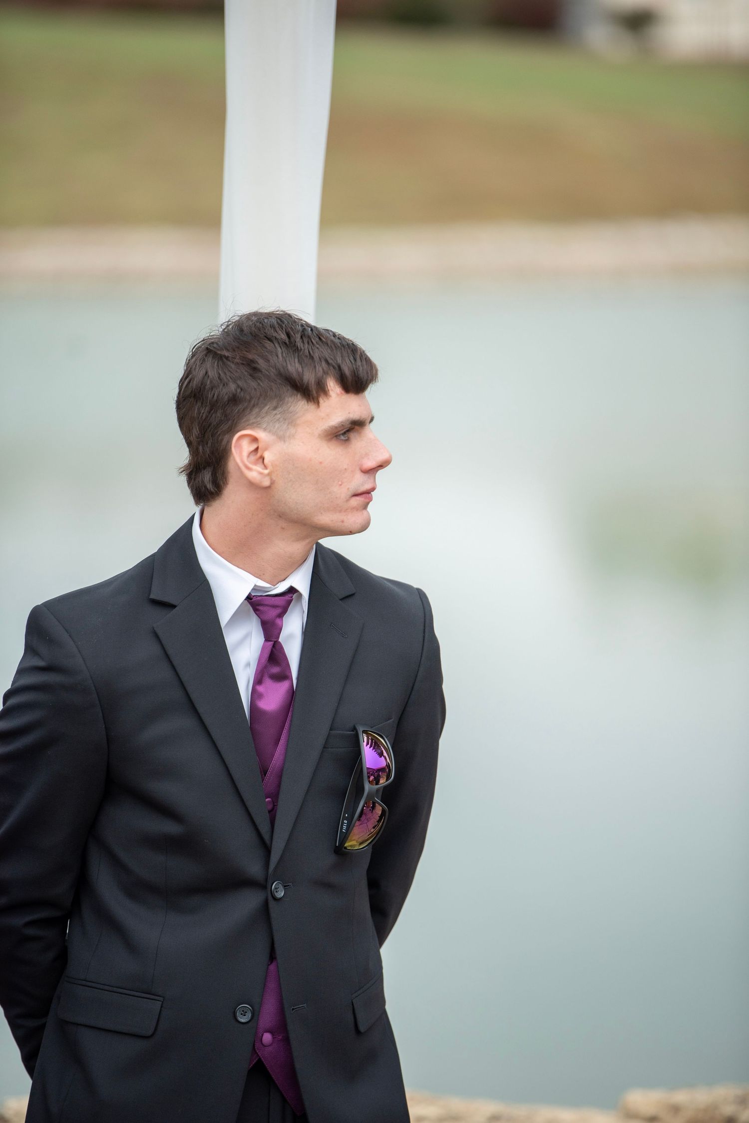 Side profile of groomsman in formal attire against blurred outdoor background.