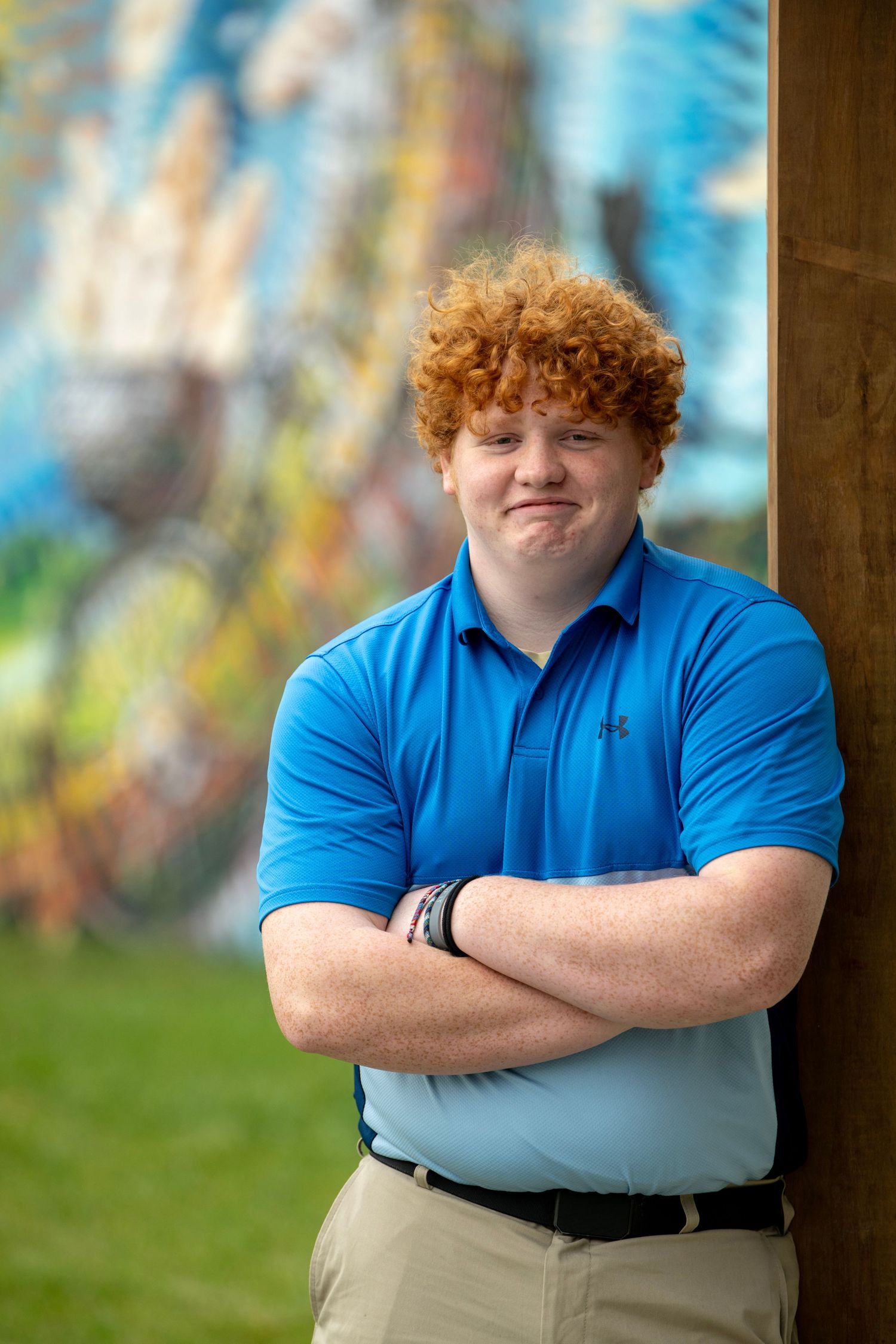 Confident pose with crossed arms in blue polo and khakis against artistic backdrop.