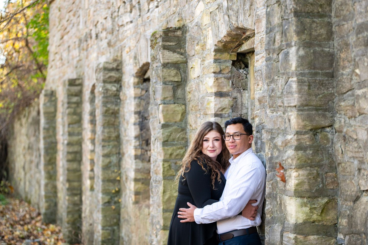 Stone pillars and arches frame romantic moment in fall setting.