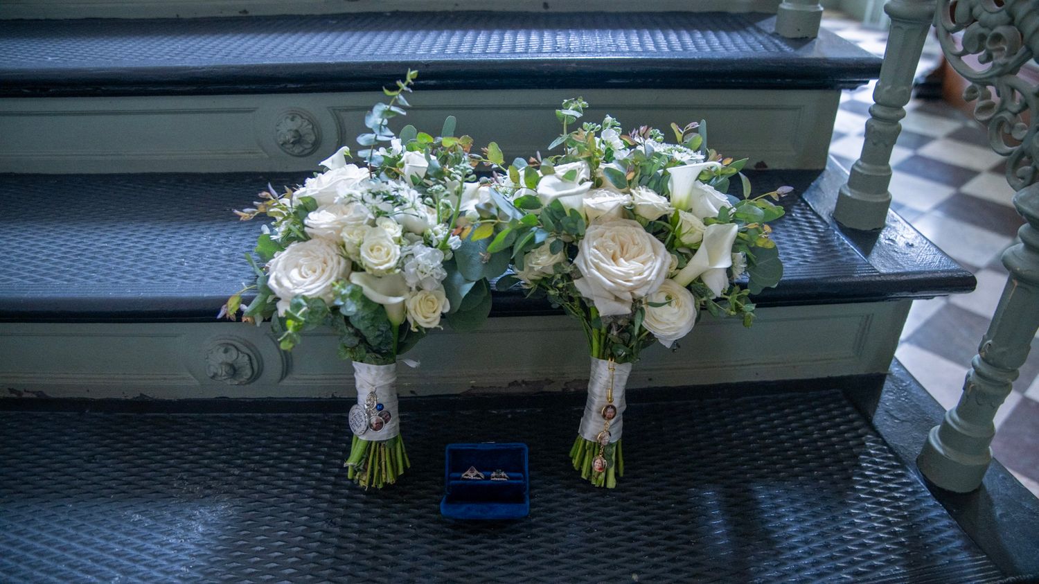 White floral wedding bouquets resting beside a blue ring box on stone steps.