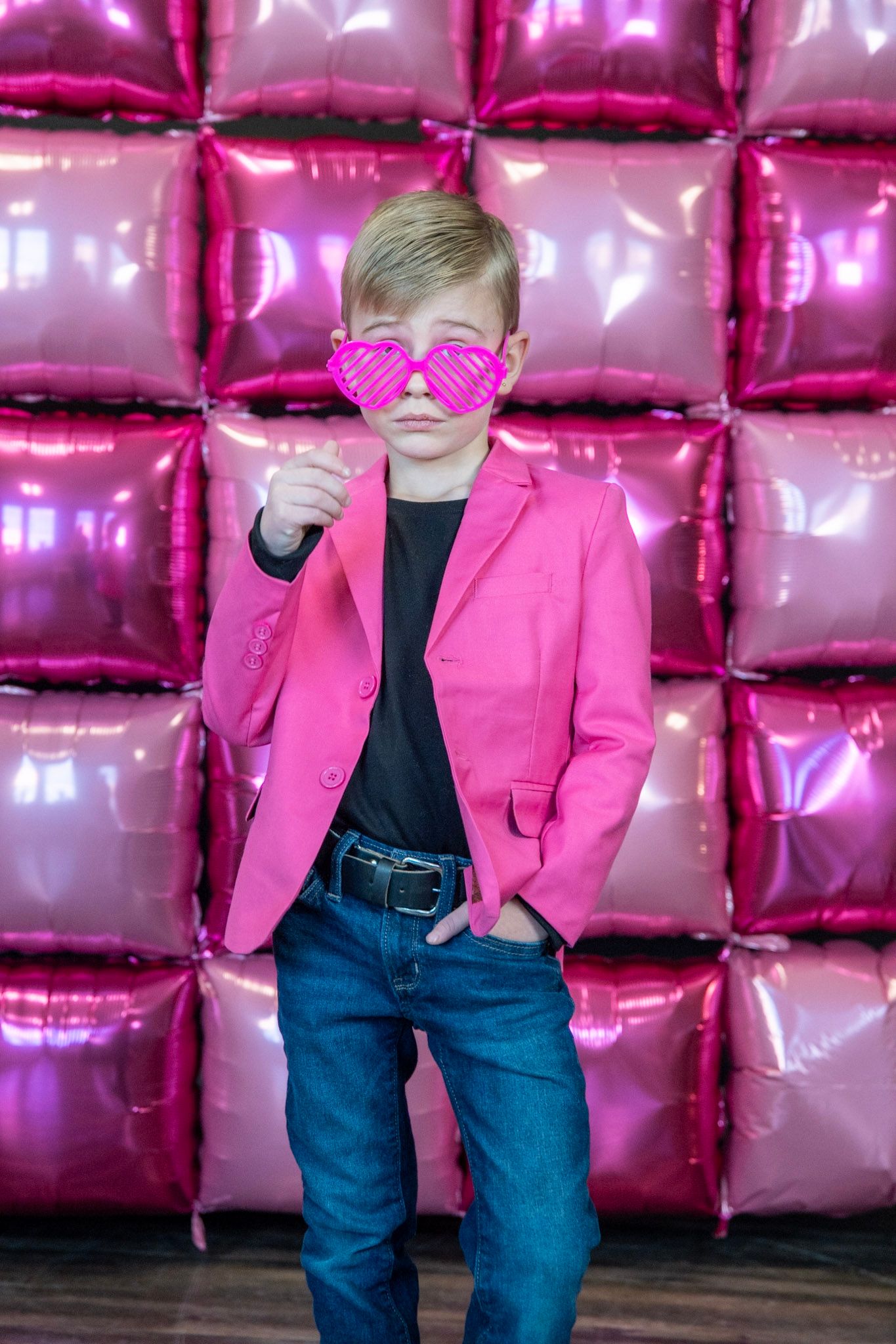 Playful poses against metallic pink balloon wall wearing bright pink jacket and jeans.