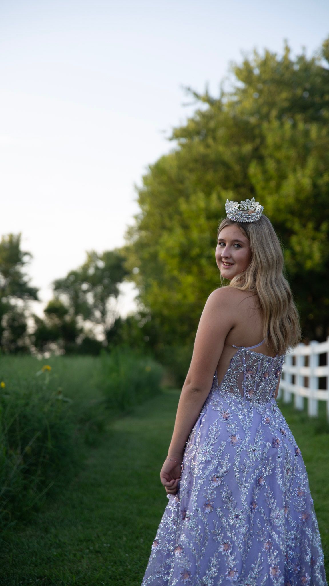 A flowing purple sequined gown photographed near a white fence in an outdoor setting.