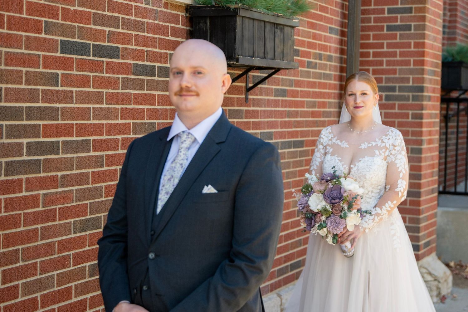 Wedding party poses against brick wall exterior during formal photos.