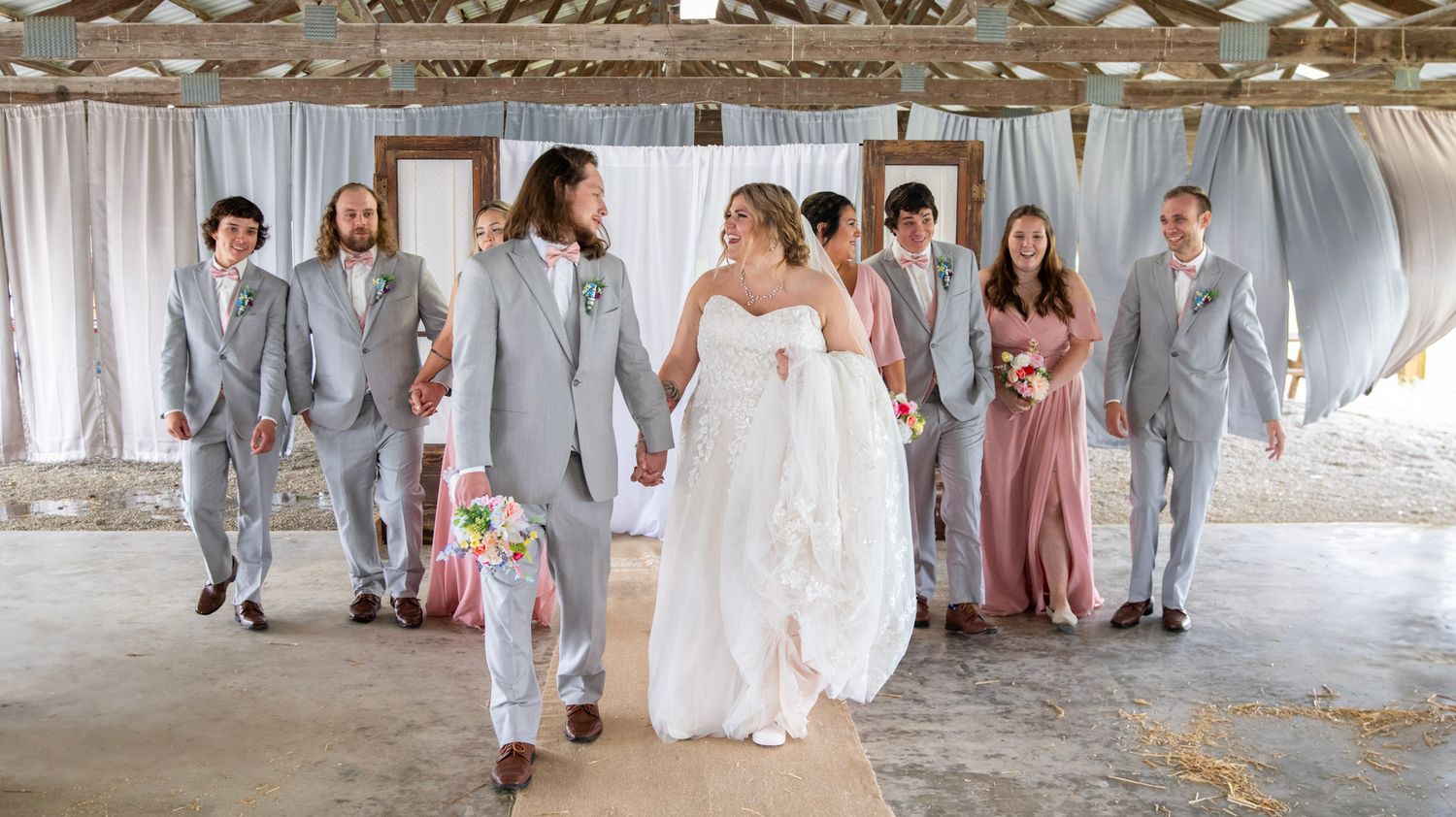 Wedding party members pose in a mix of pink bridesmaid dresses and light grey suits.