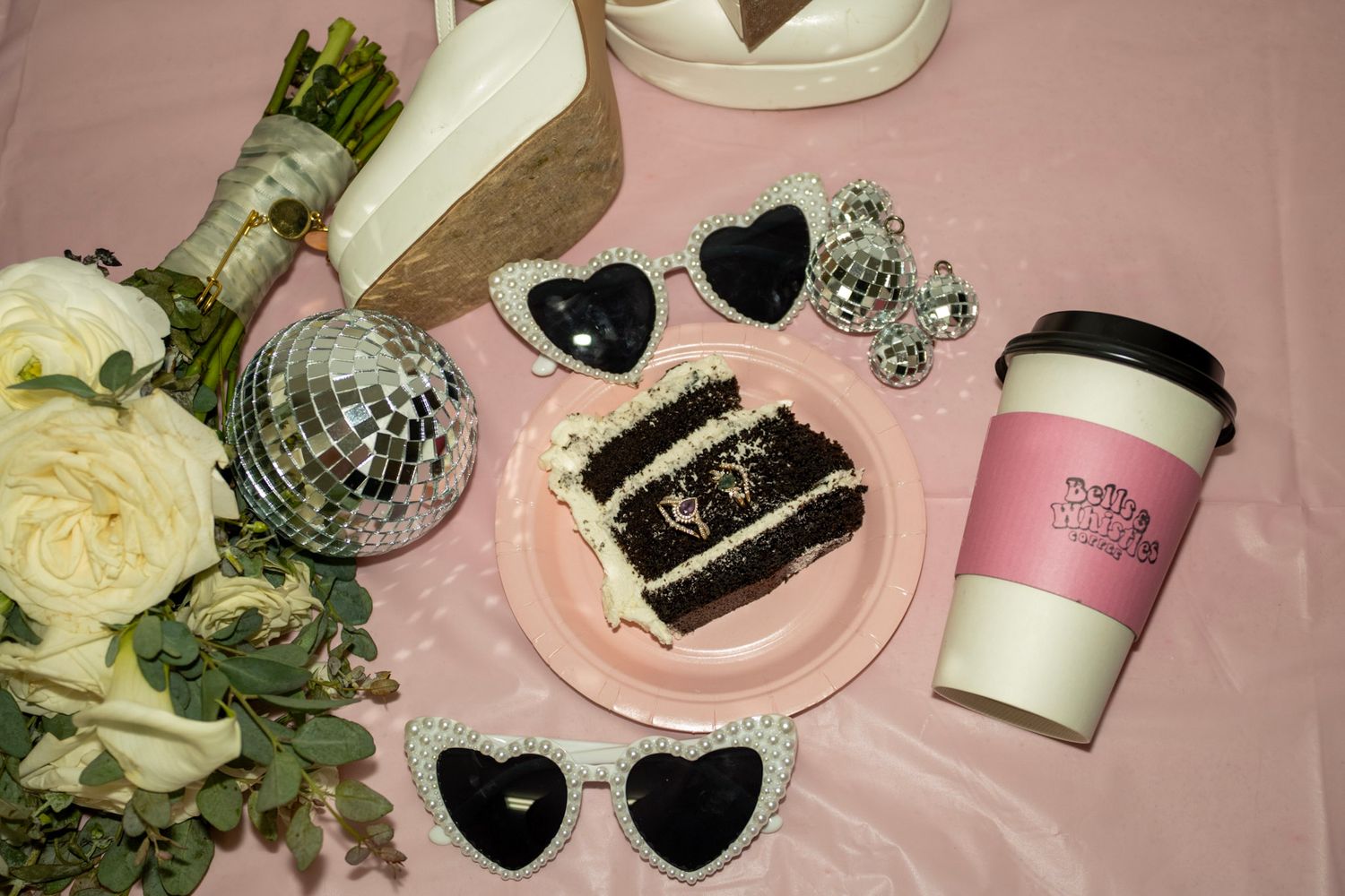 Vintage styled flat lay with heart sunglasses, cake slice, roses and pink coffee cup.
