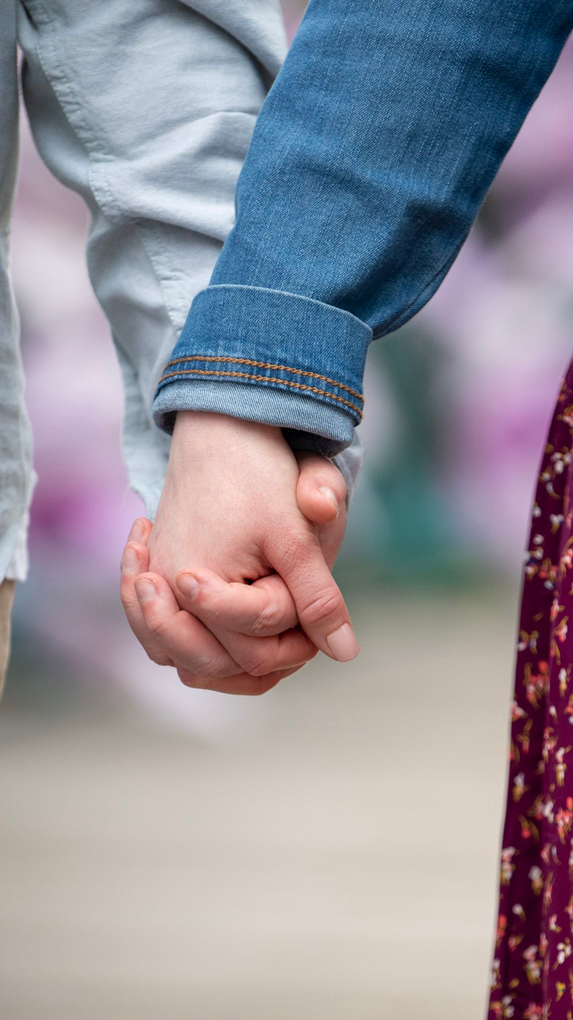 Close-up of two people holding hands while wearing casual denim and light colored clothing.