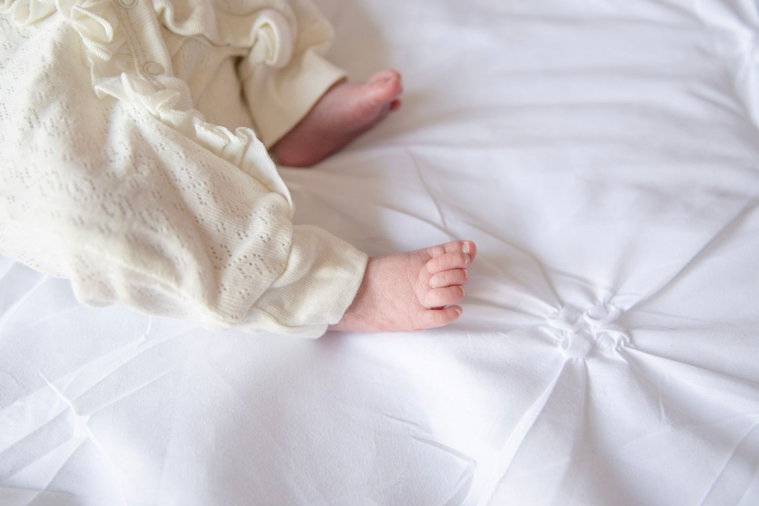 Close-up of baby's feet and legs on white quilted background.