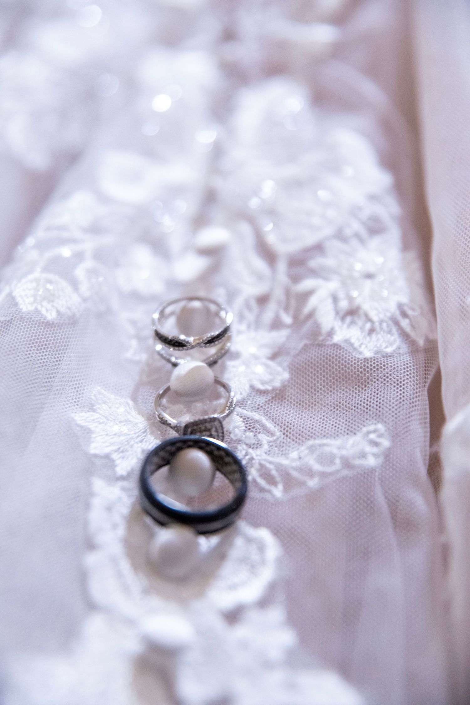 Wedding rings photographed in macro detail on delicate white lace fabric.
