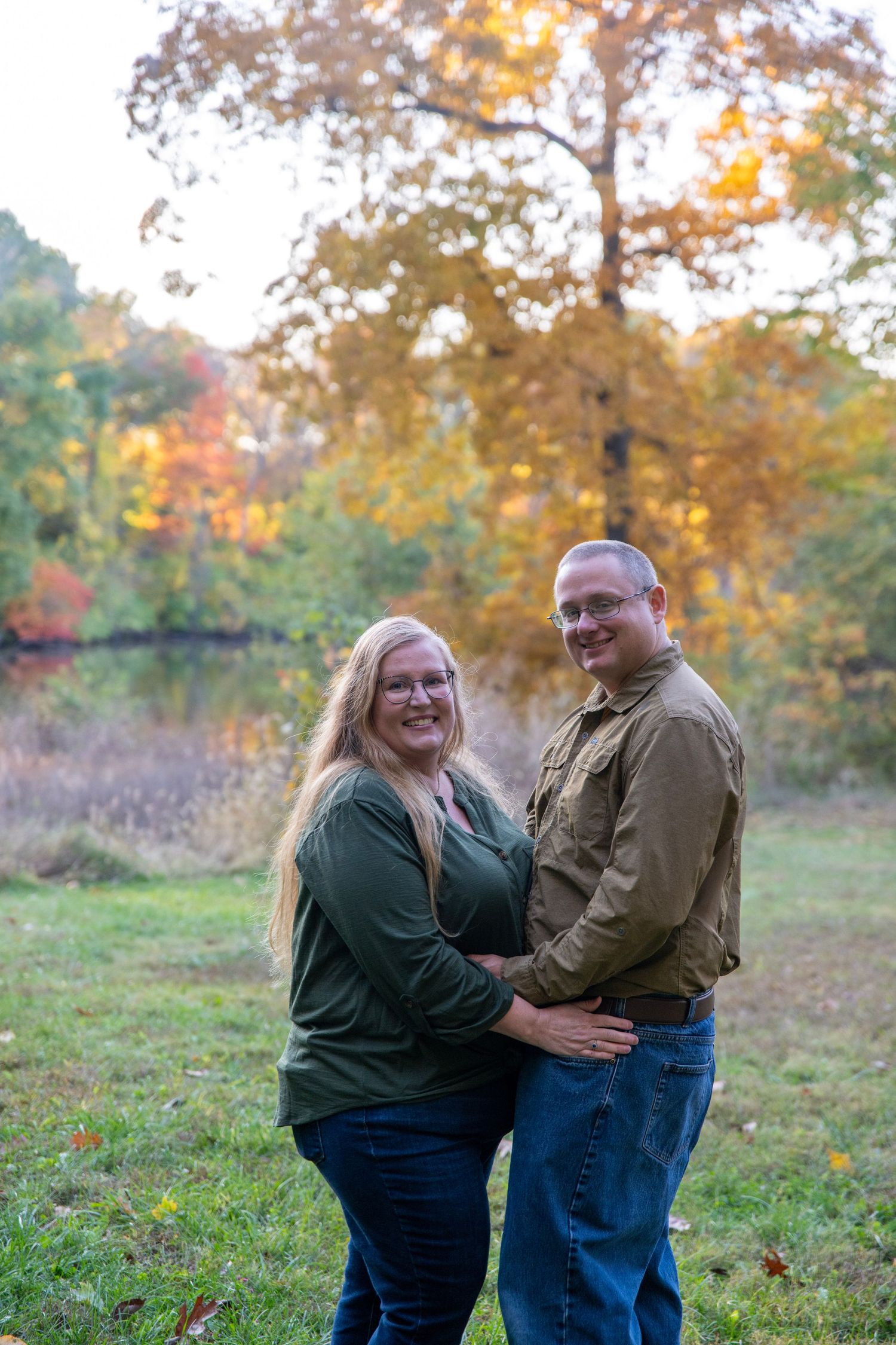 A couple shares an intimate moment outdoors during autumn with golden foliage in the background.