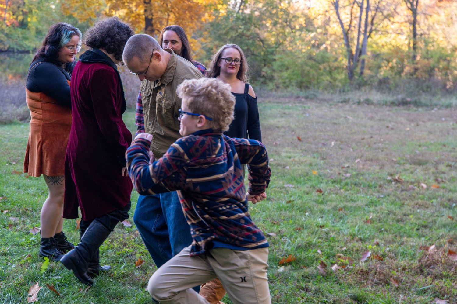 Family members laugh together during casual outdoor photo session in autumn setting.