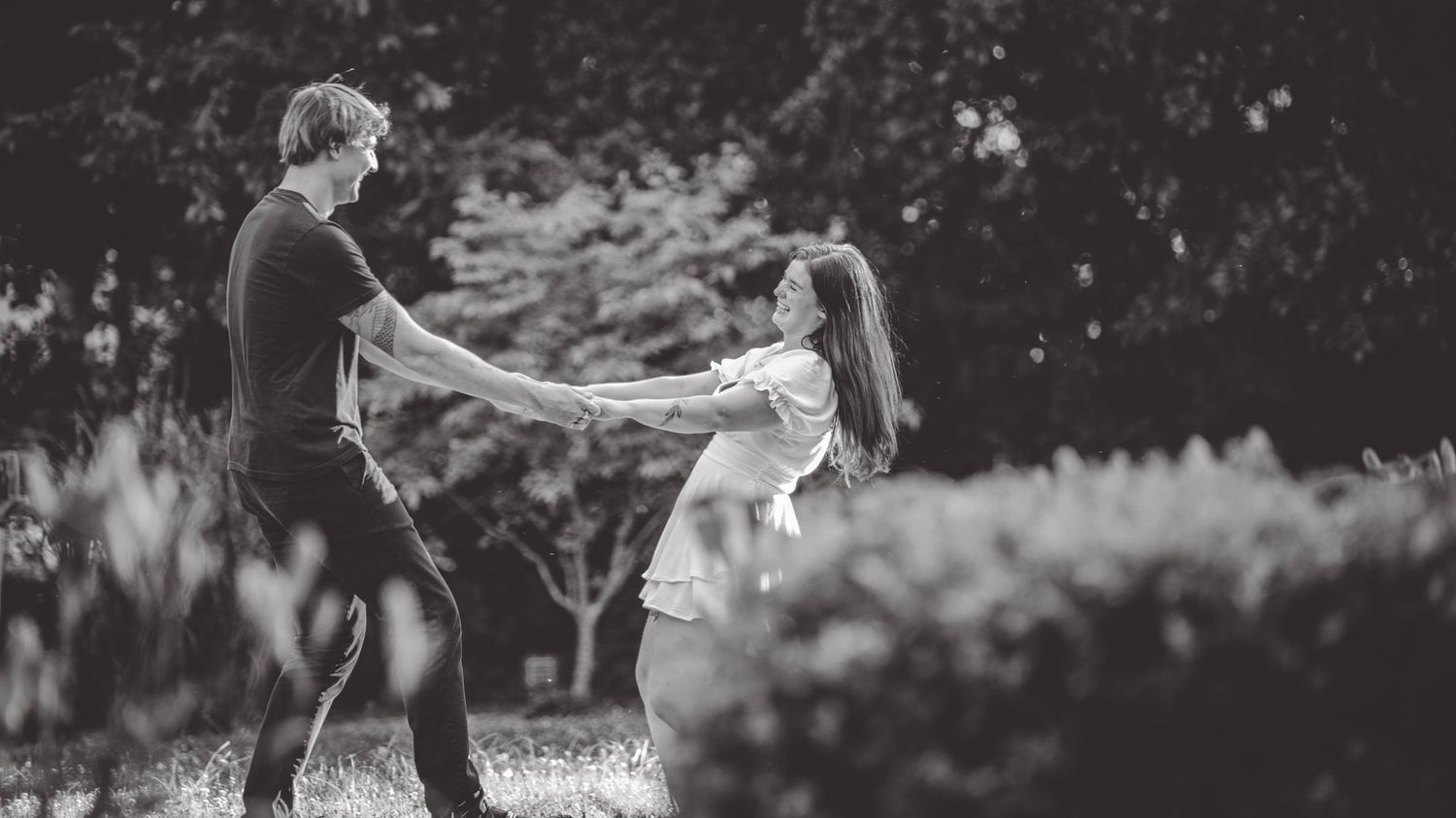 A playful couple spins together in a black and white photo outdoors.