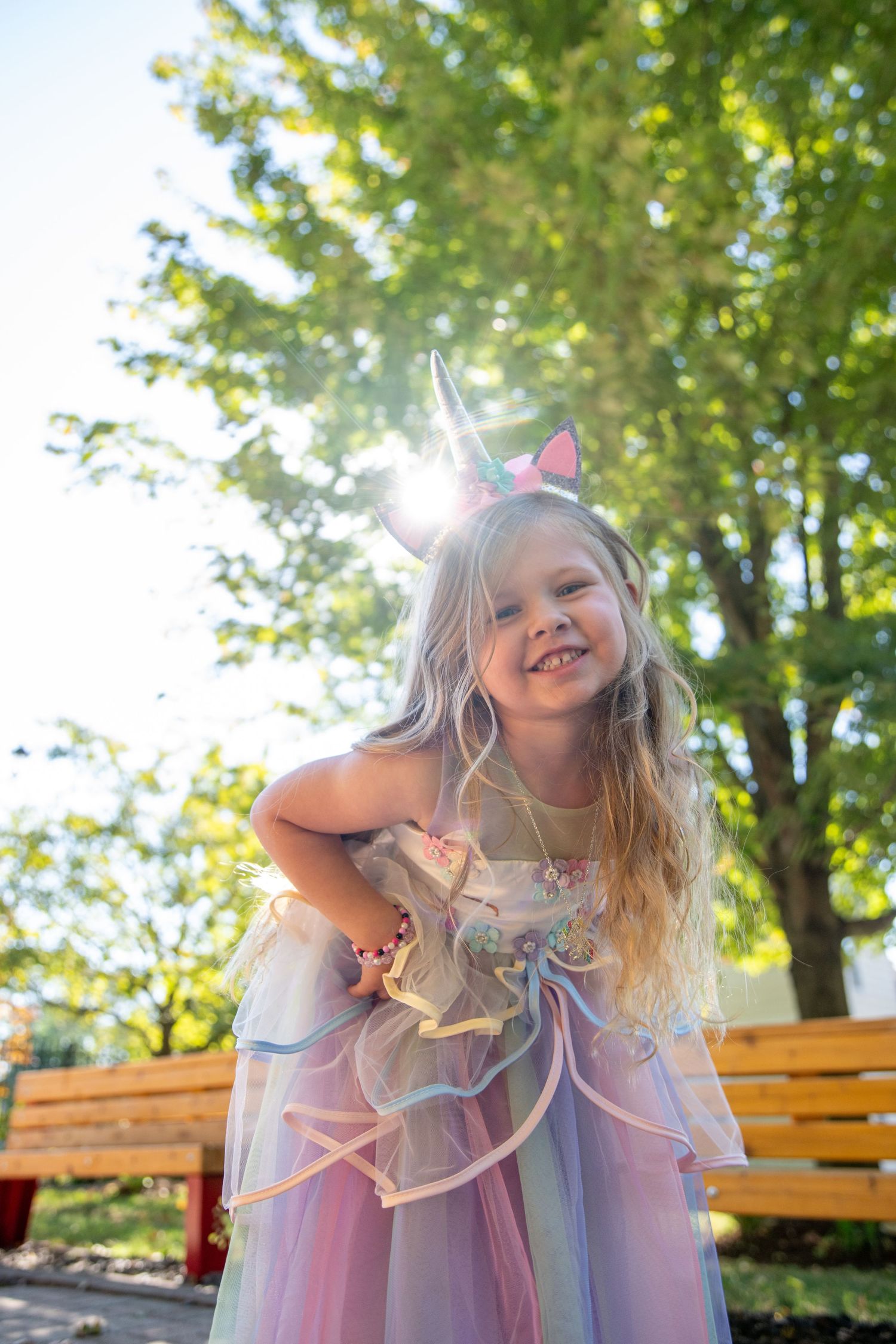 Whimsical portraits of a child in pastel dress with unicorn accessories against green foliage.