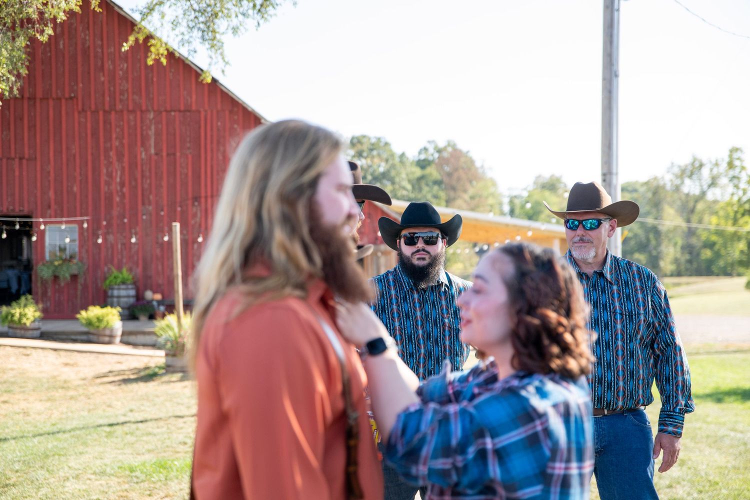 People gathered outdoors near a red barn on a sunny day.